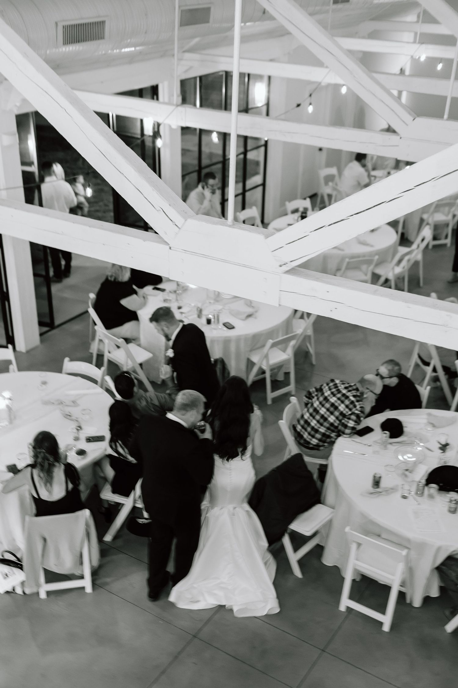 Wedding reception guests seated at tables under white draped fabric ceiling decorations at an indoor venue.