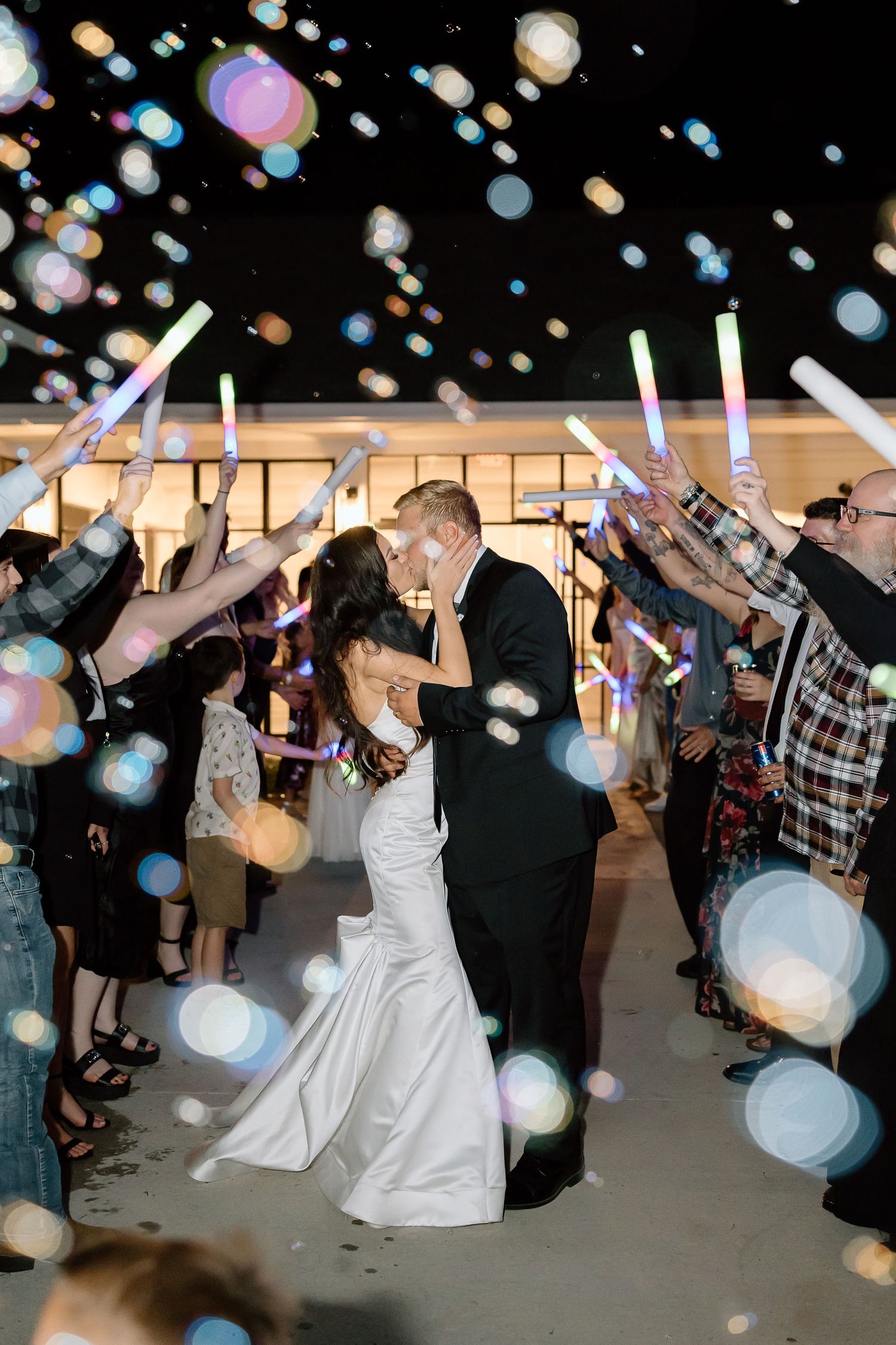 Wedding guests dance and celebrate under floating bubbles during a lively reception party.