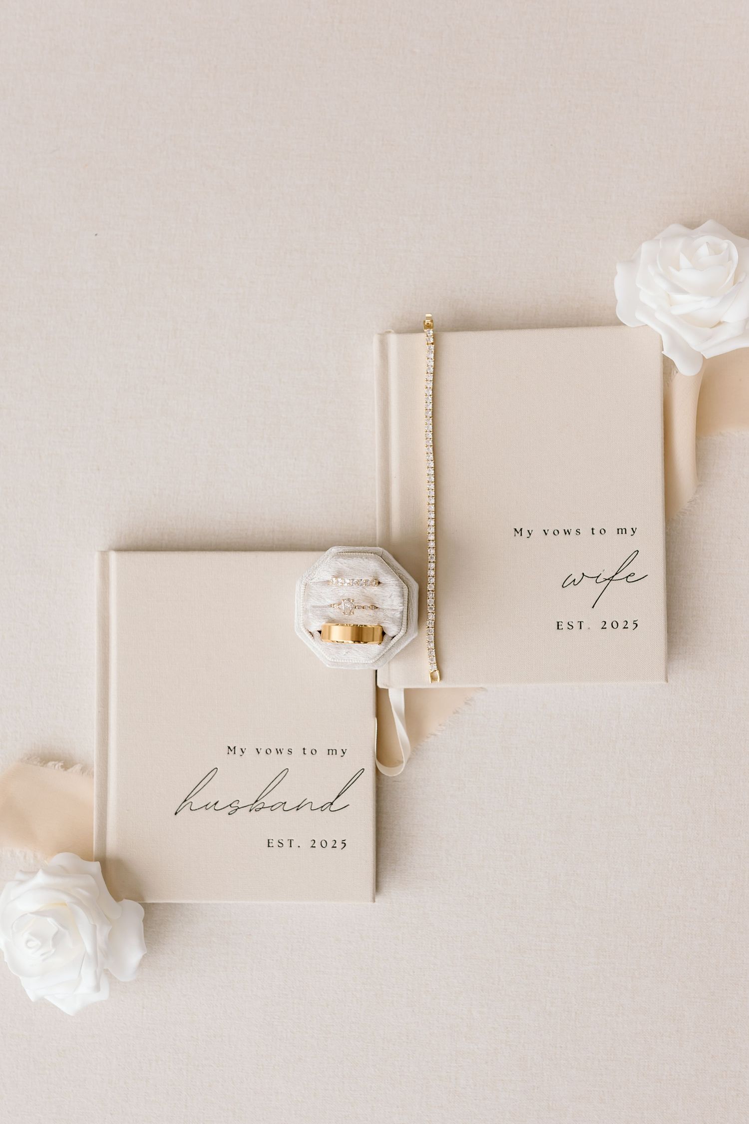 Minimalist wedding vow books in cream color with gold foil lettering arranged on light beige background.