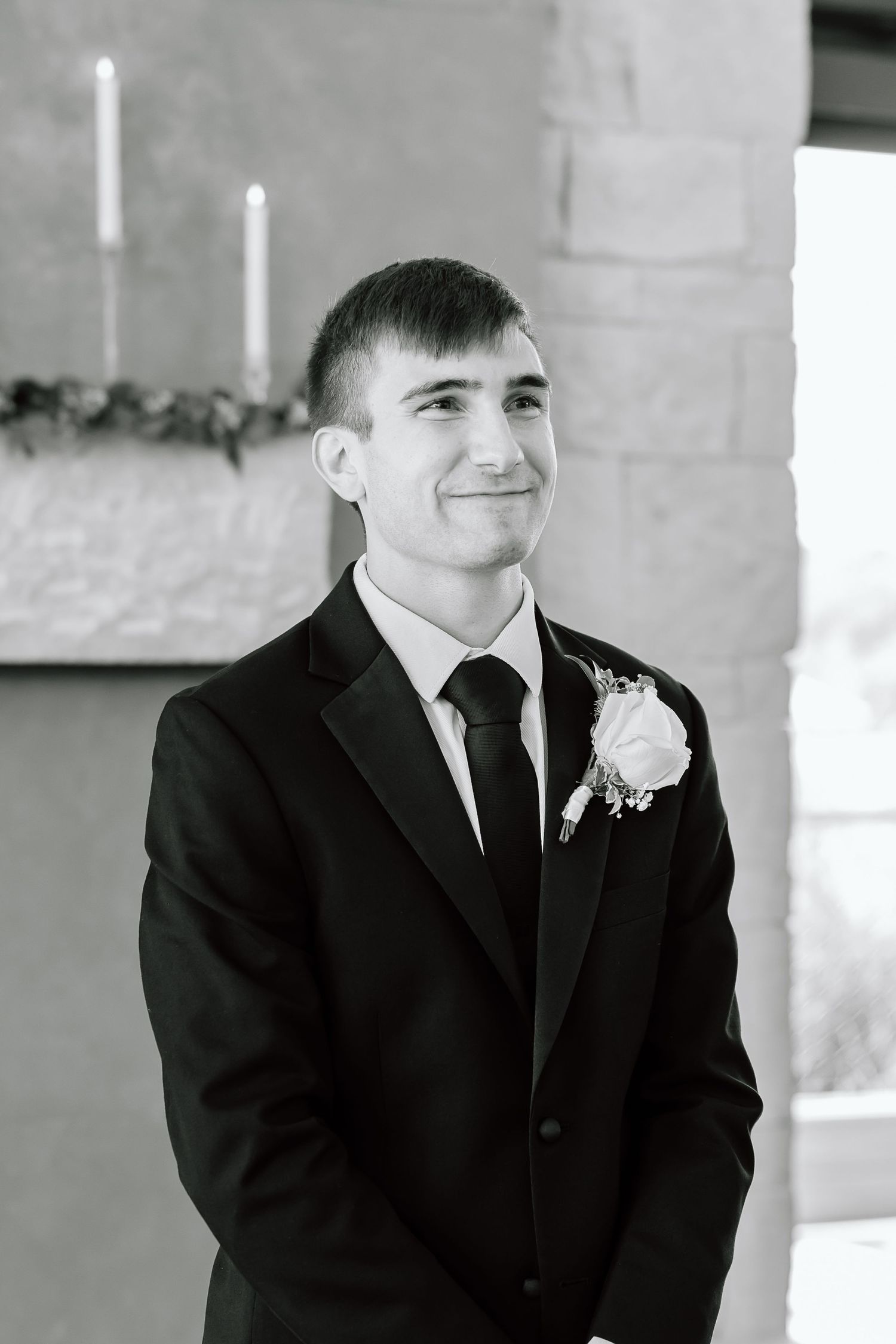 Black and white portrait of groomsman at wedding wearing black suit with boutonniere and smiling.