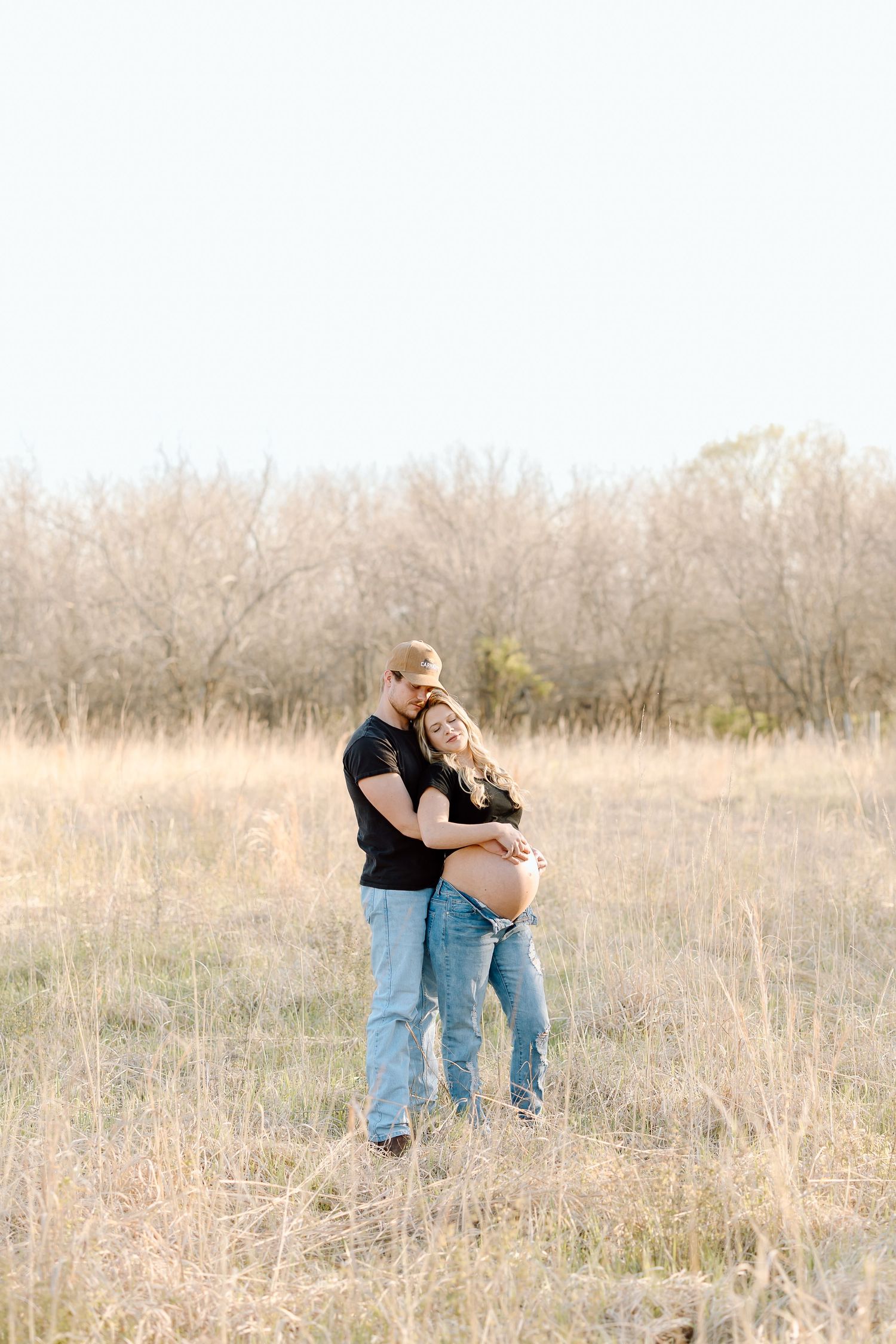 A couple embraces in a romantic moment while standing in a golden autumn field at sunset.