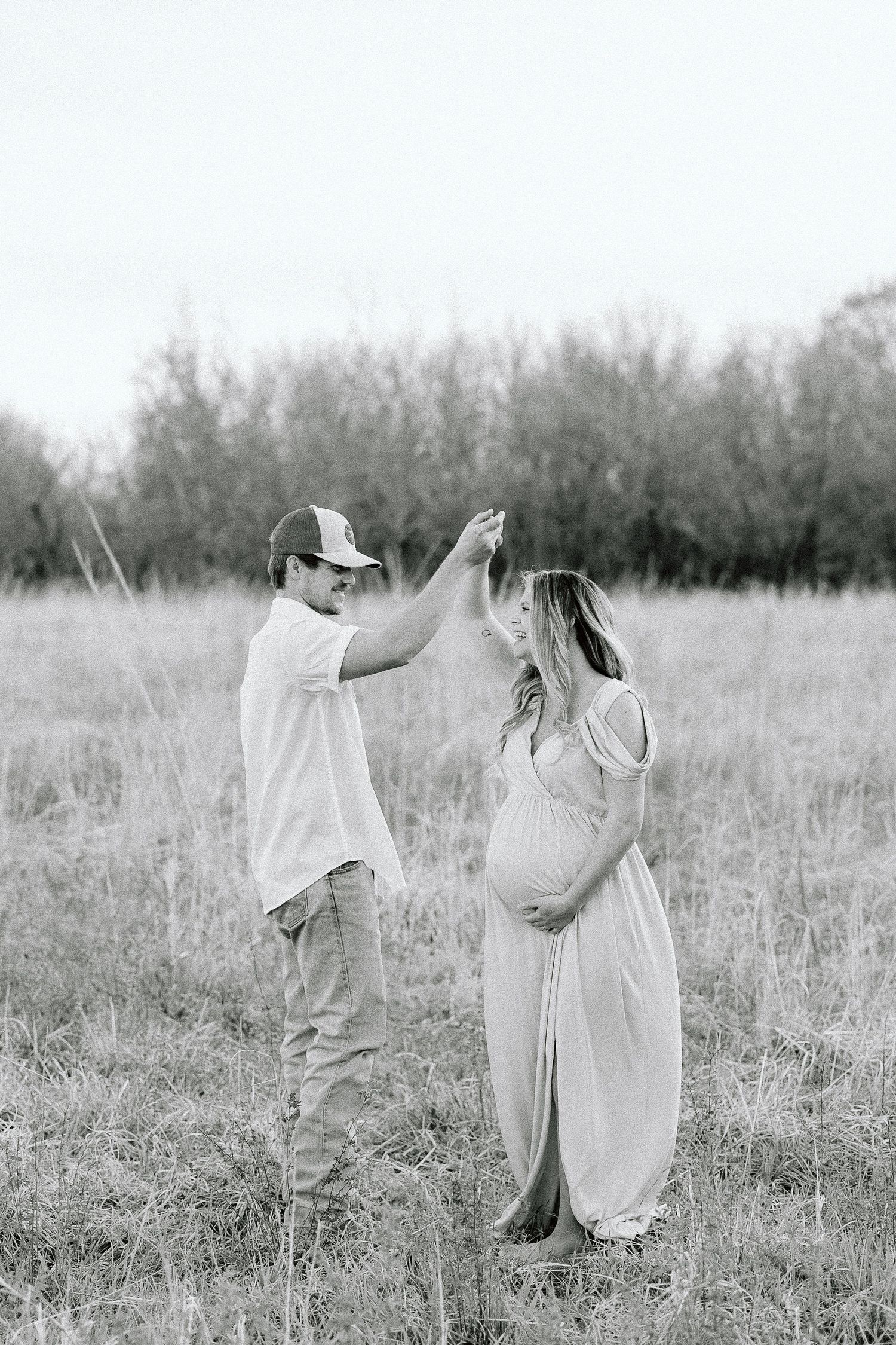 A couple shares a tender moment in a field as they celebrate an upcoming arrival with a black and white photo shoot.