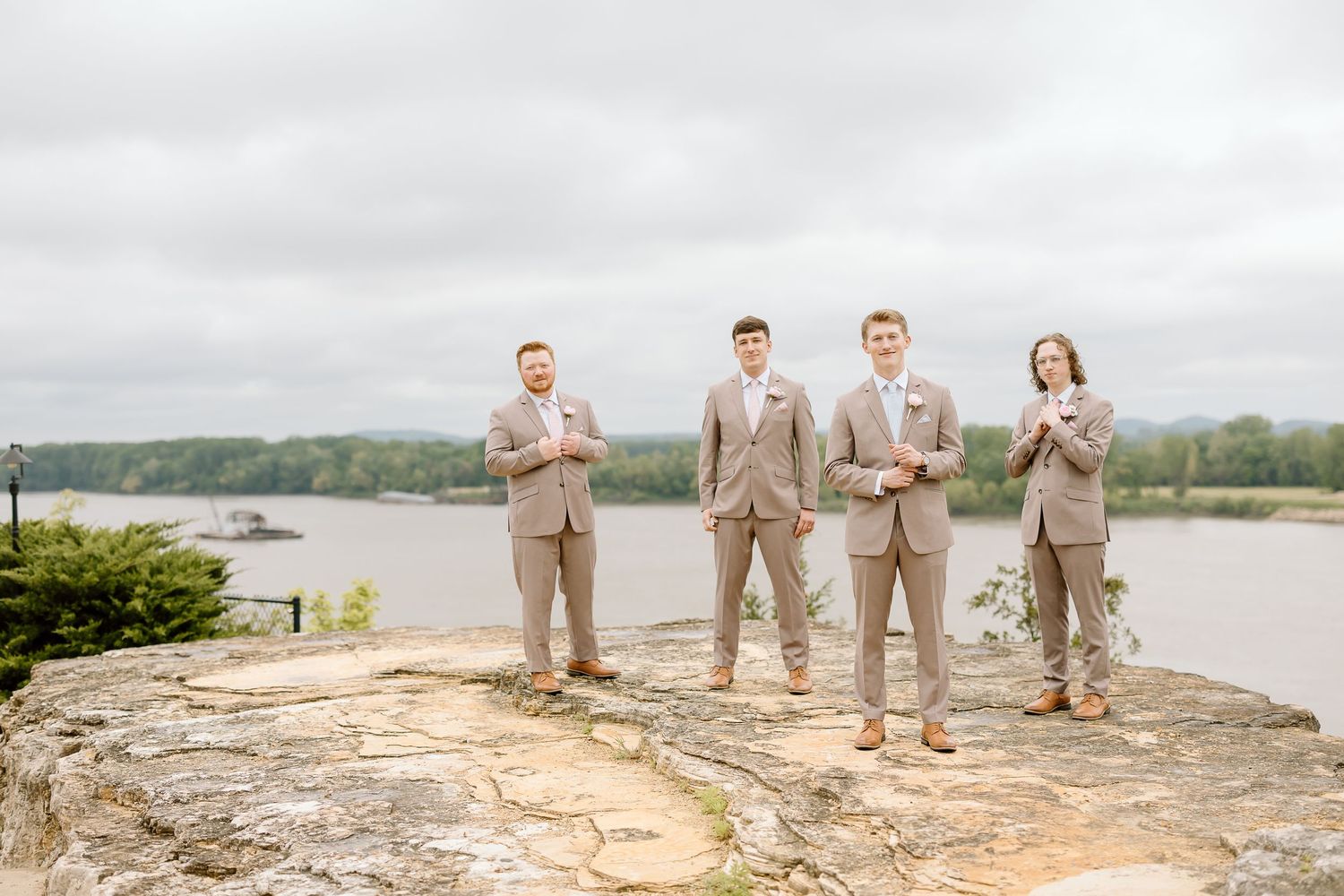 Wedding party in tan suits poses together on a rocky coastal outcrop overlooking the ocean on an overcast day.