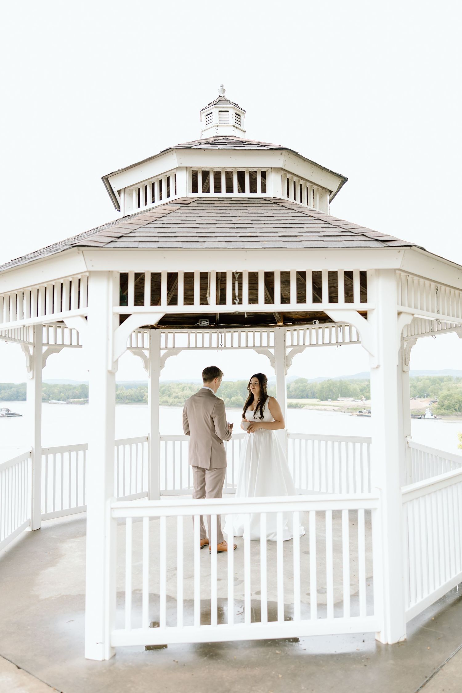 White wooden gazebo overlooking water with people enjoying the scenic view from different angles.