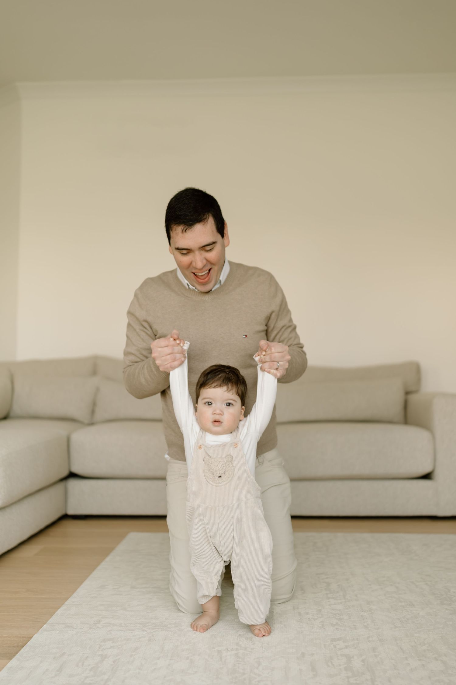 A sequence of photos showing a parent helping a baby learn to walk on a beige carpet in front of a light gray sofa.