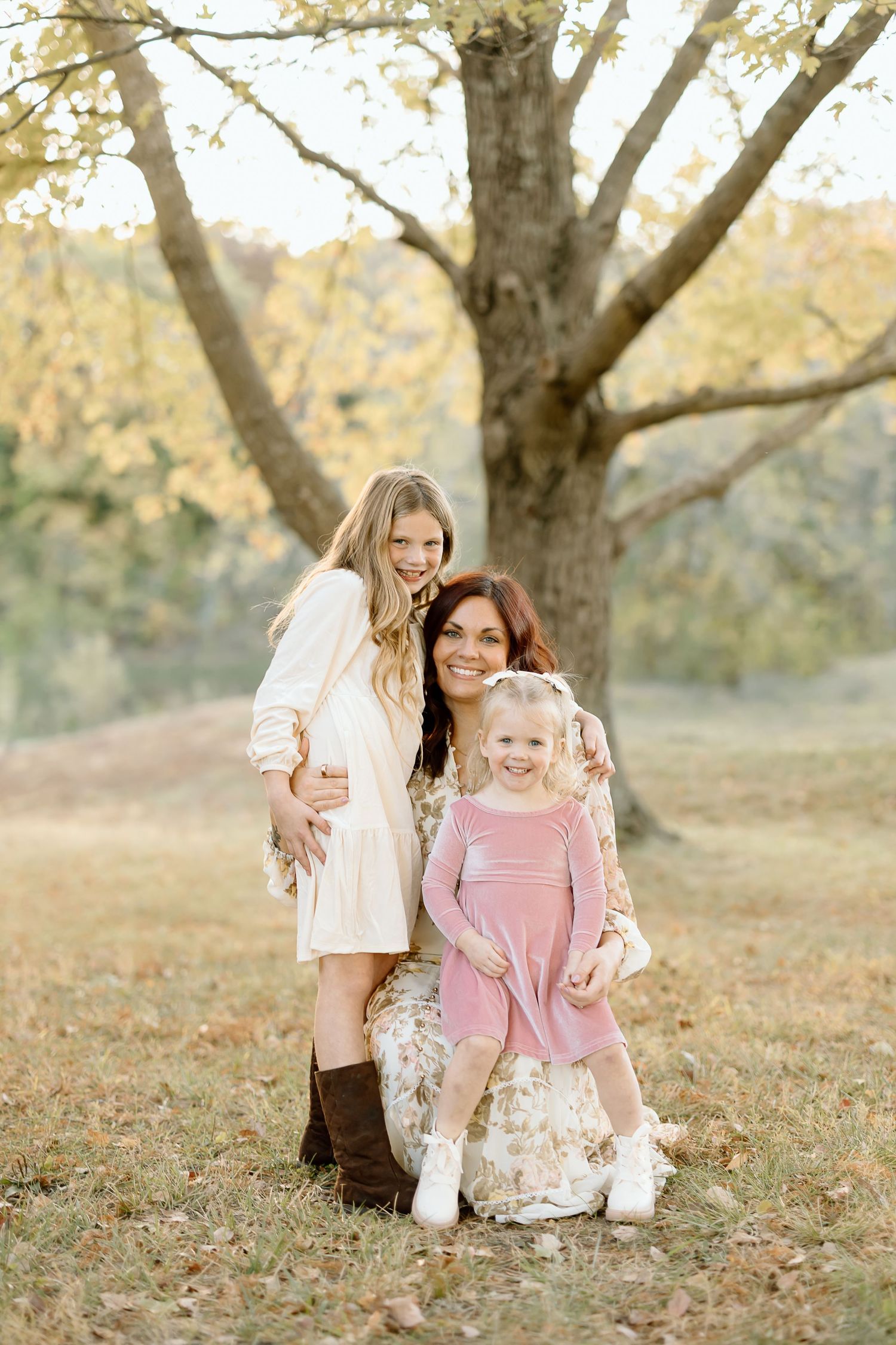 Mother and daughter share playful moments together in an autumn setting under a large tree.