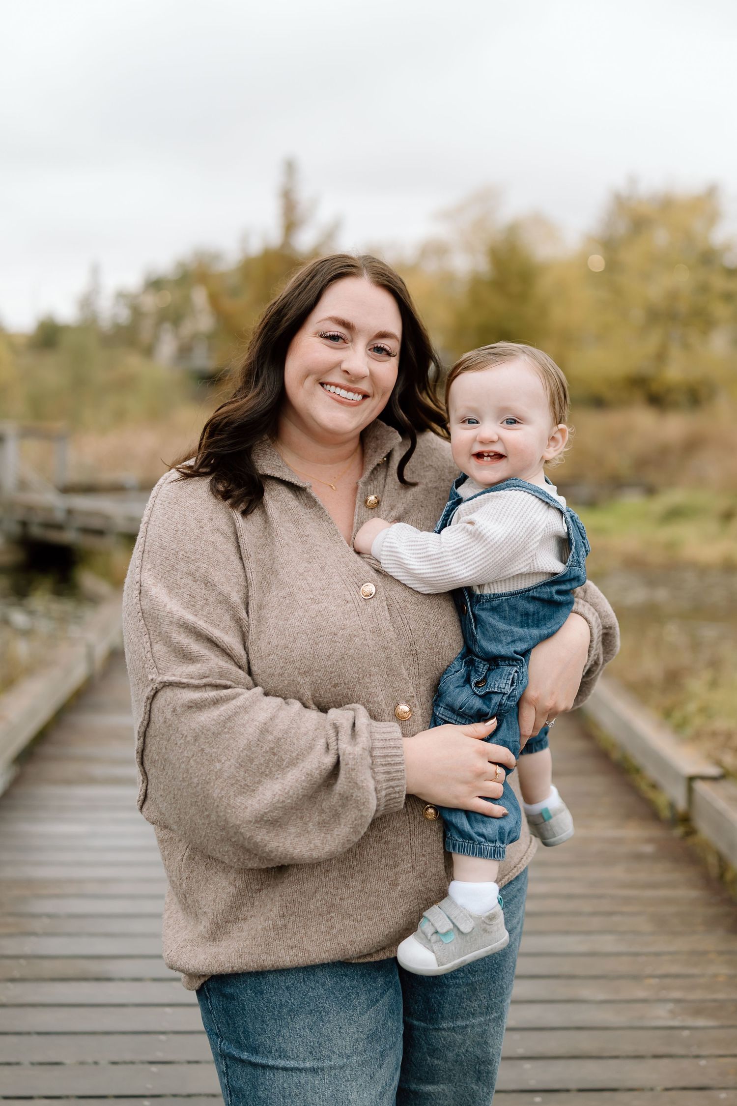 Joyful candid moments shared between parent and child while standing on a wooden walkway in natural outdoor setting.