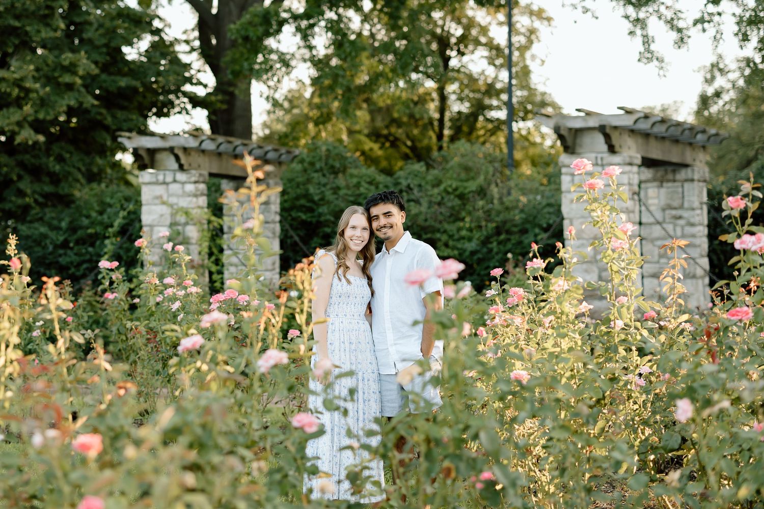 Couple shares romantic moments in a blooming rose garden with stone architecture in the background.