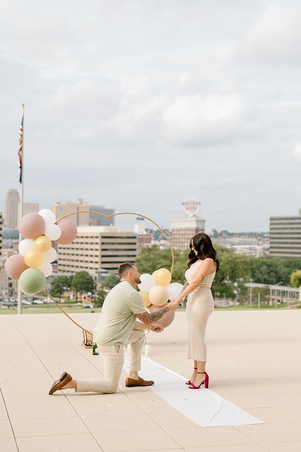 A series of romantic picnic engagement photos showing a couple with balloons on a sunny day in an urban setting.