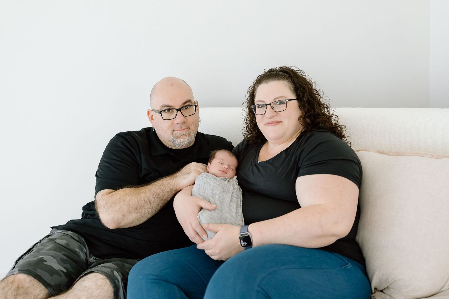 Family relaxing together on a light gray couch in a bright, minimalist living room setting.