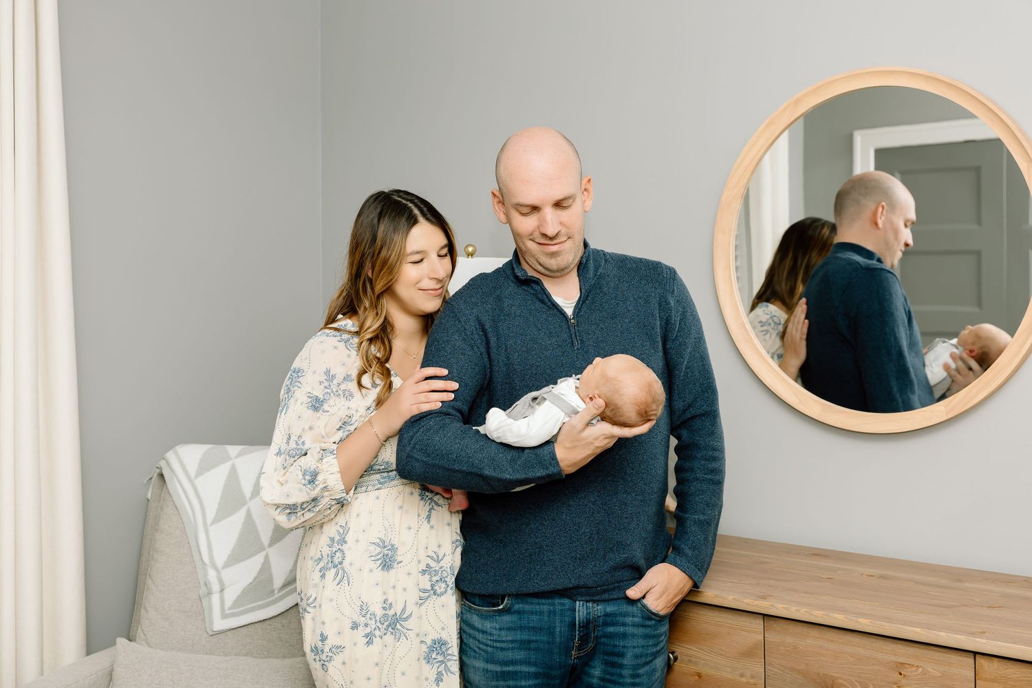 A family poses together in a modern home interior with neutral decor and a round mirror on the wall.