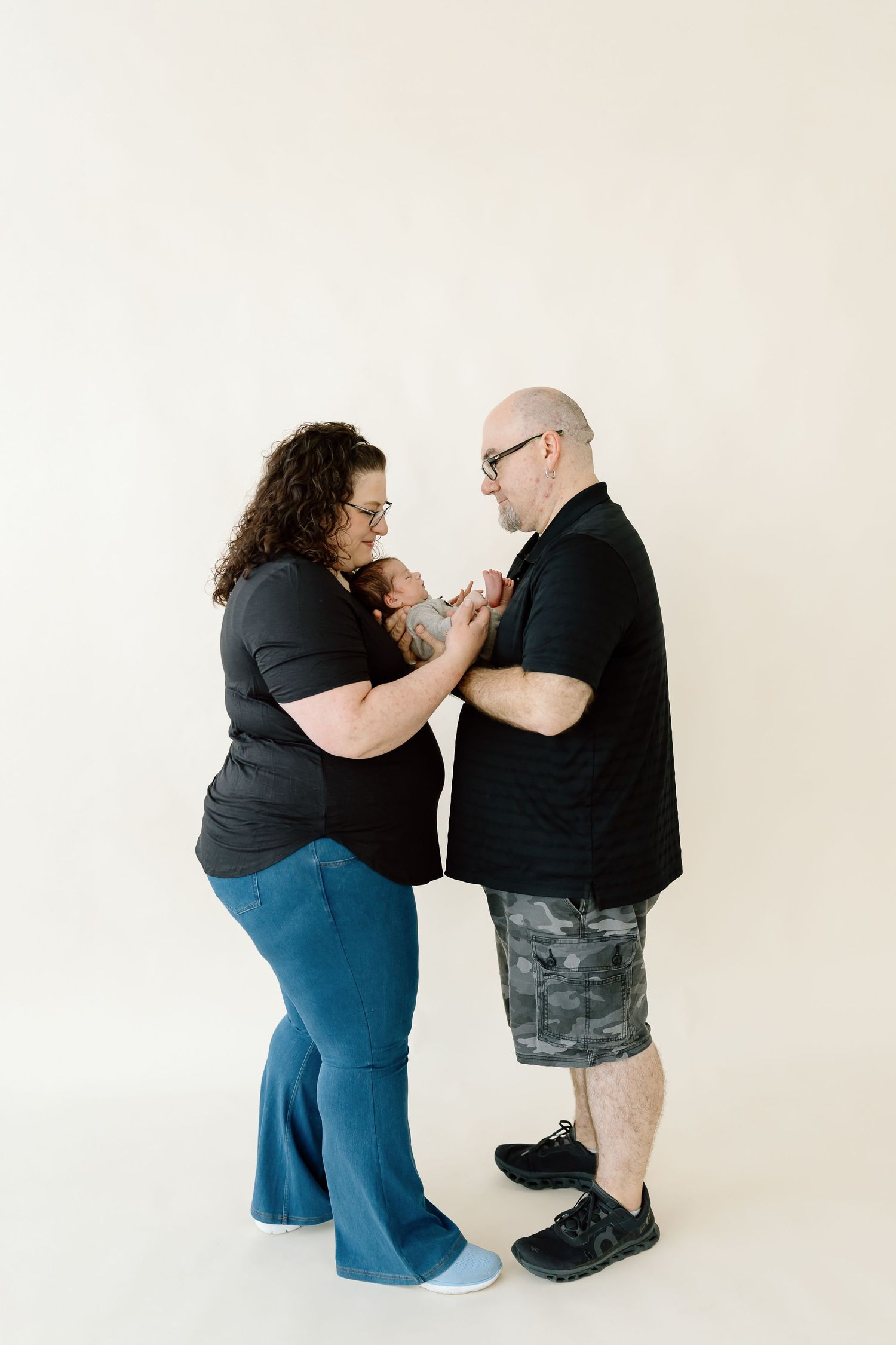 A couple in black clothing shares an intimate moment during a professional photo shoot against a light background.