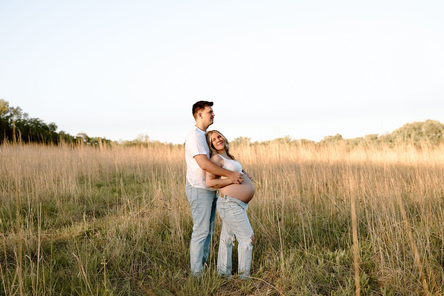 Romantic couple embraces in tall golden grass field during sunset photoshoot.