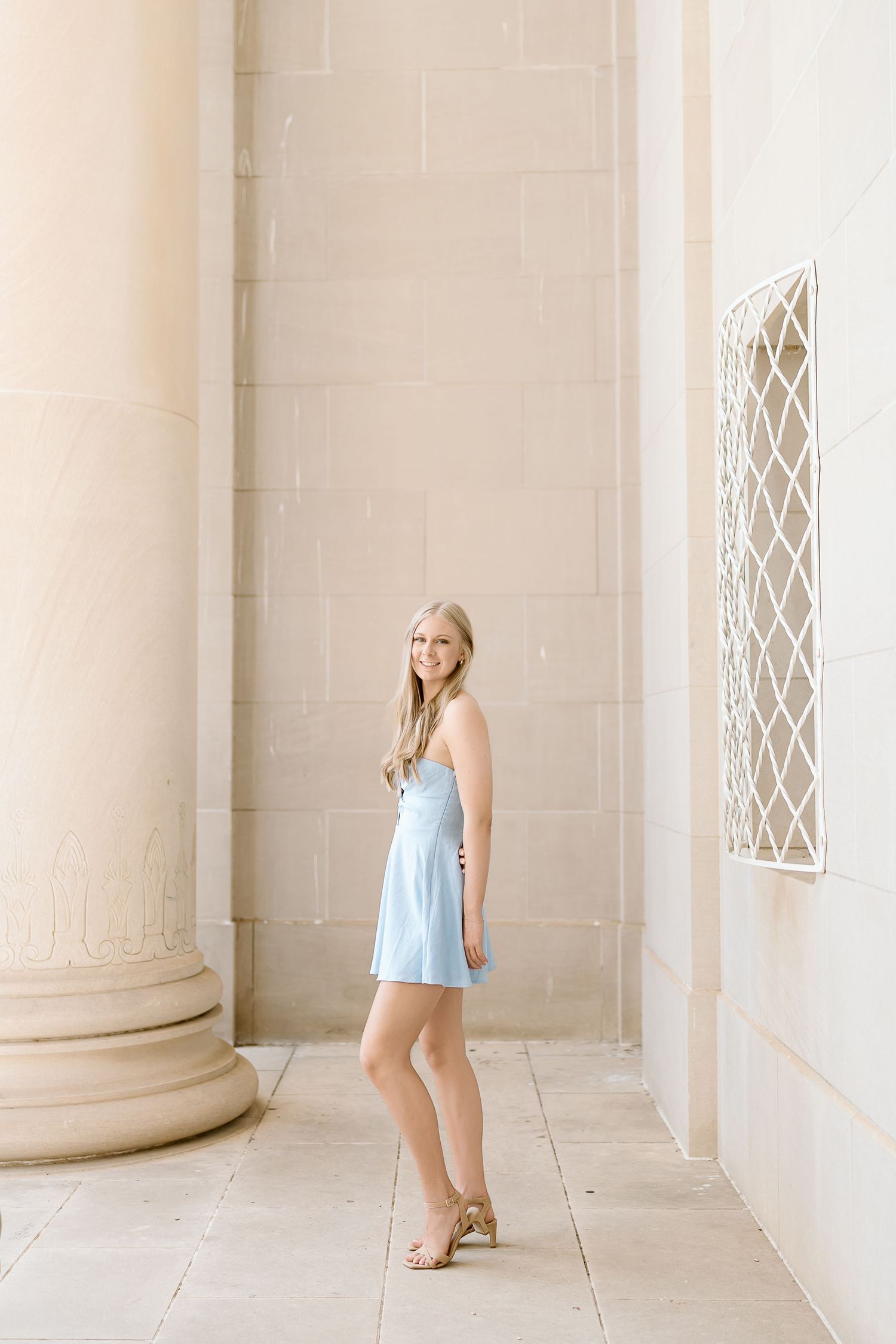 A light blue sundress stands out against white stone columns and architectural details in an elegant outdoor setting.