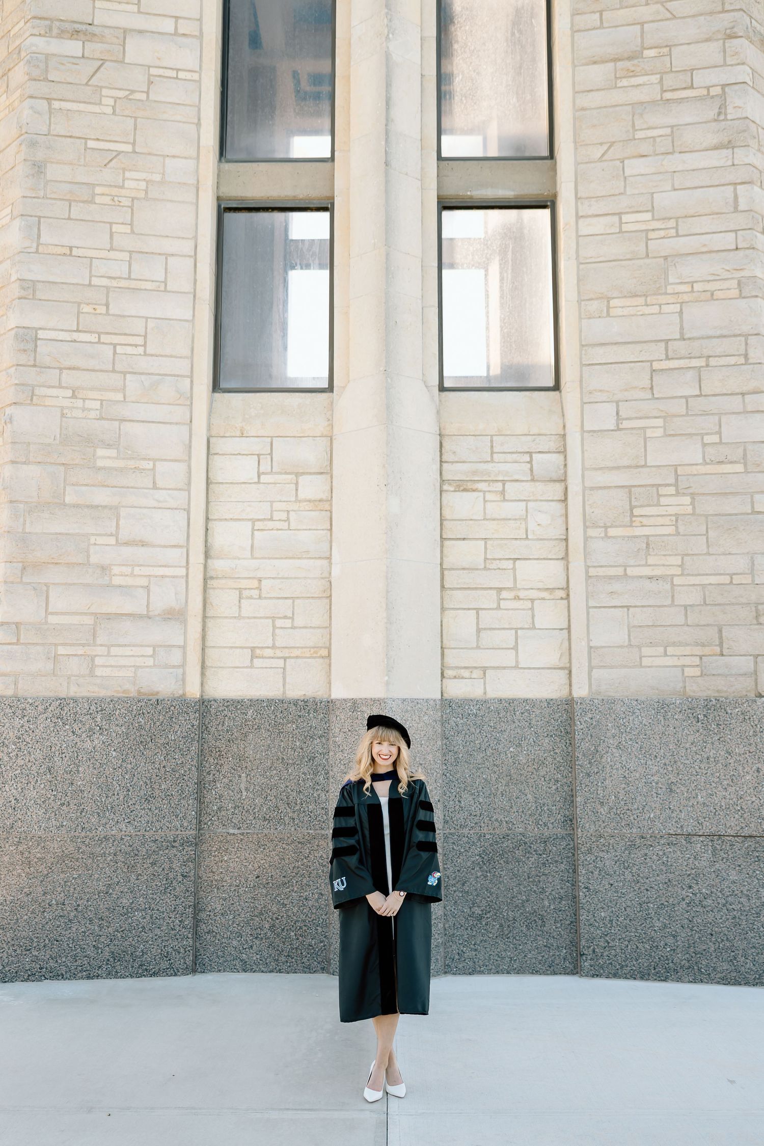 A graduate in black cap and gown stands against a light stone wall in a series of progressive poses.