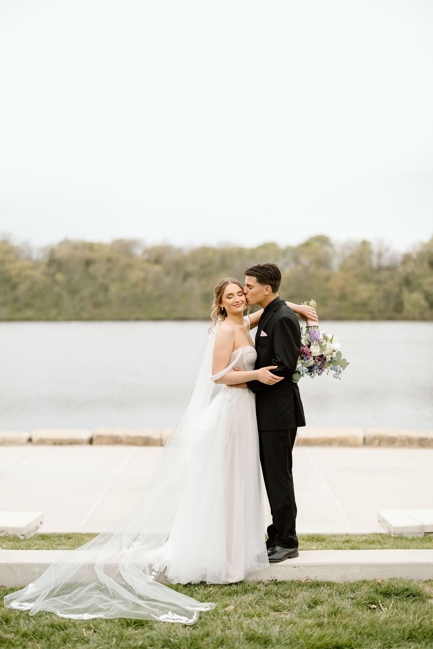 Joyful wedding couple embraces during outdoor photo session by the water.
