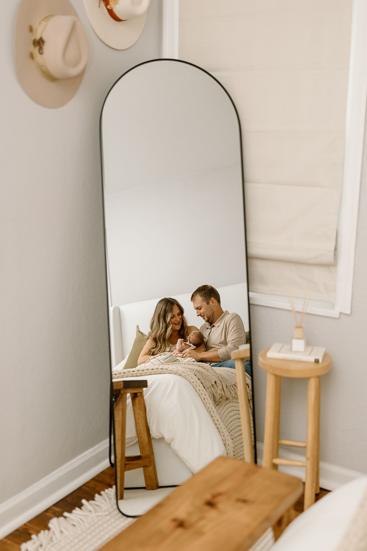 A peaceful family moment reflected in an arched floor mirror beside a wooden bench and white bedding.