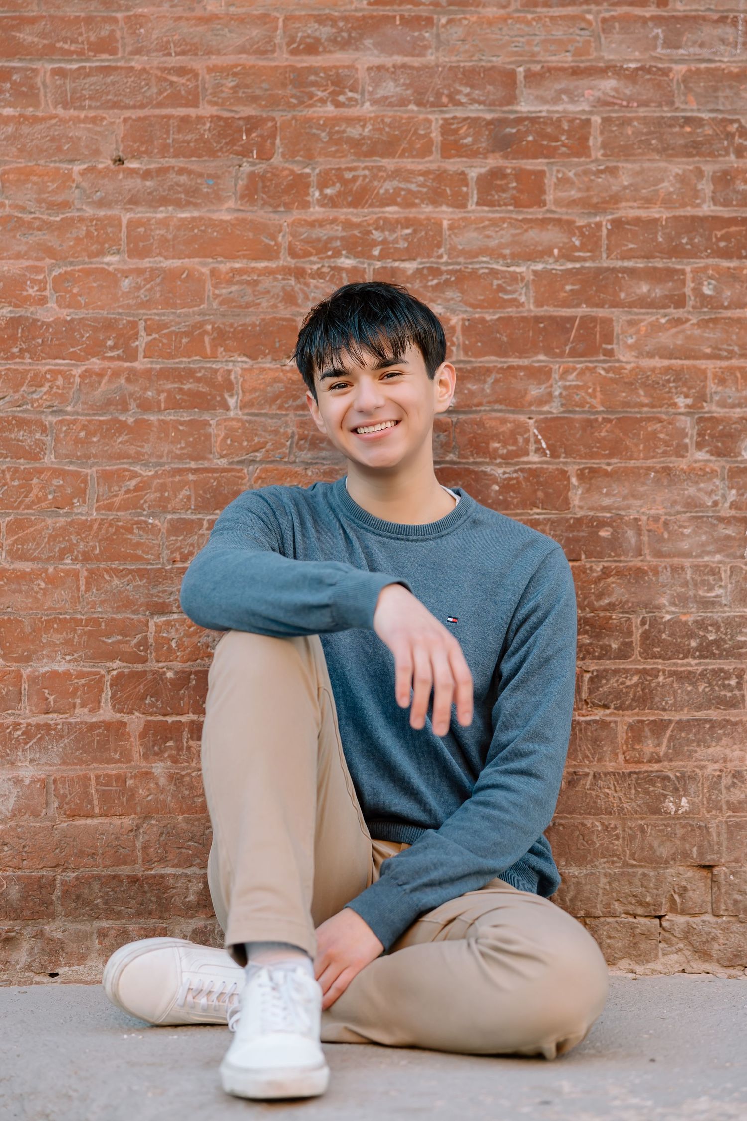 Cheerful portrait against brick wall wearing blue sweater and light pants.