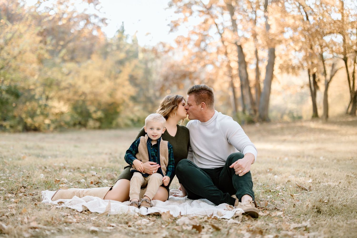 A couple shares an intimate moment while sitting on a blanket outdoors in autumn.