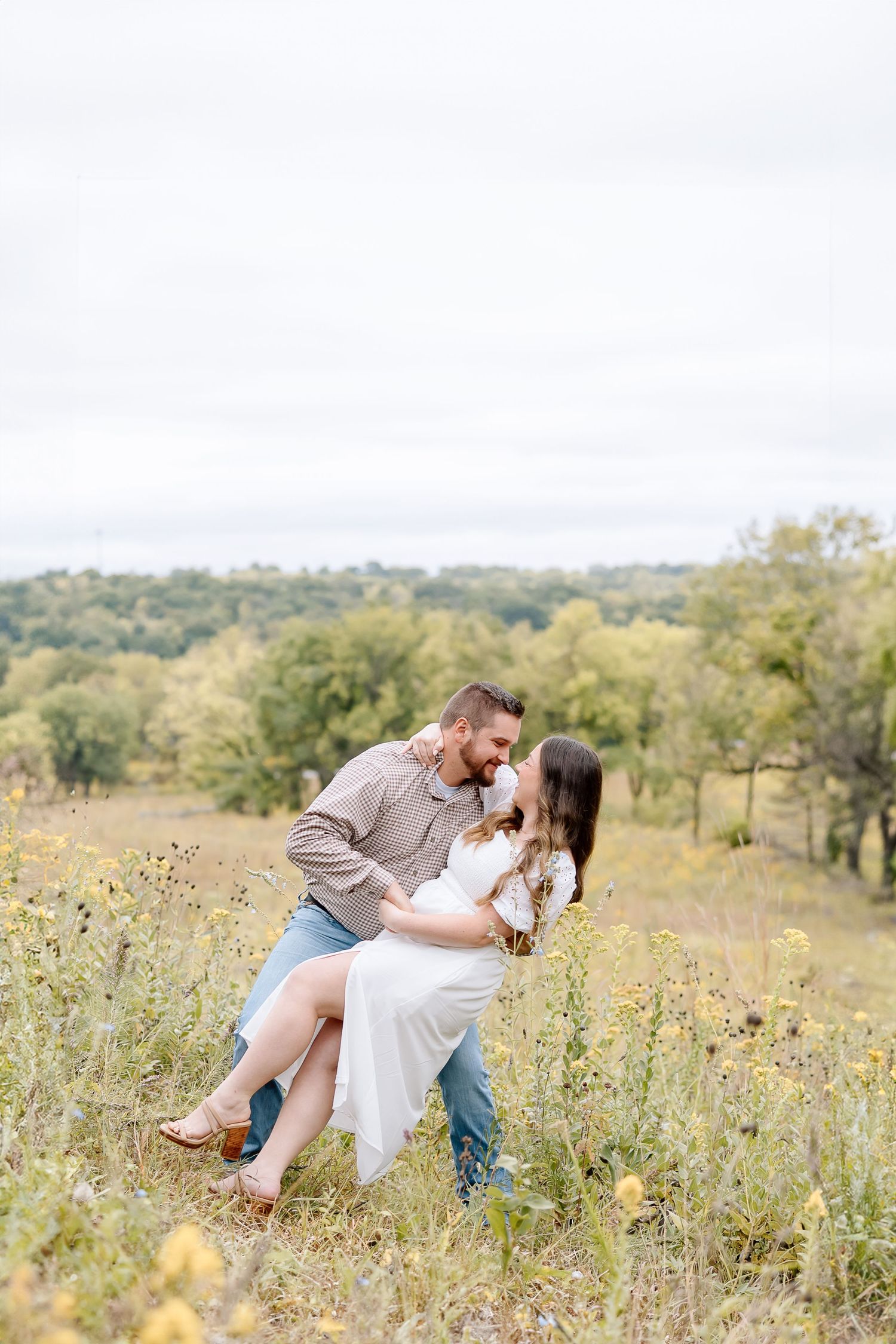 Couple sharing a romantic dip pose among yellow wildflowers in a hilltop meadow.