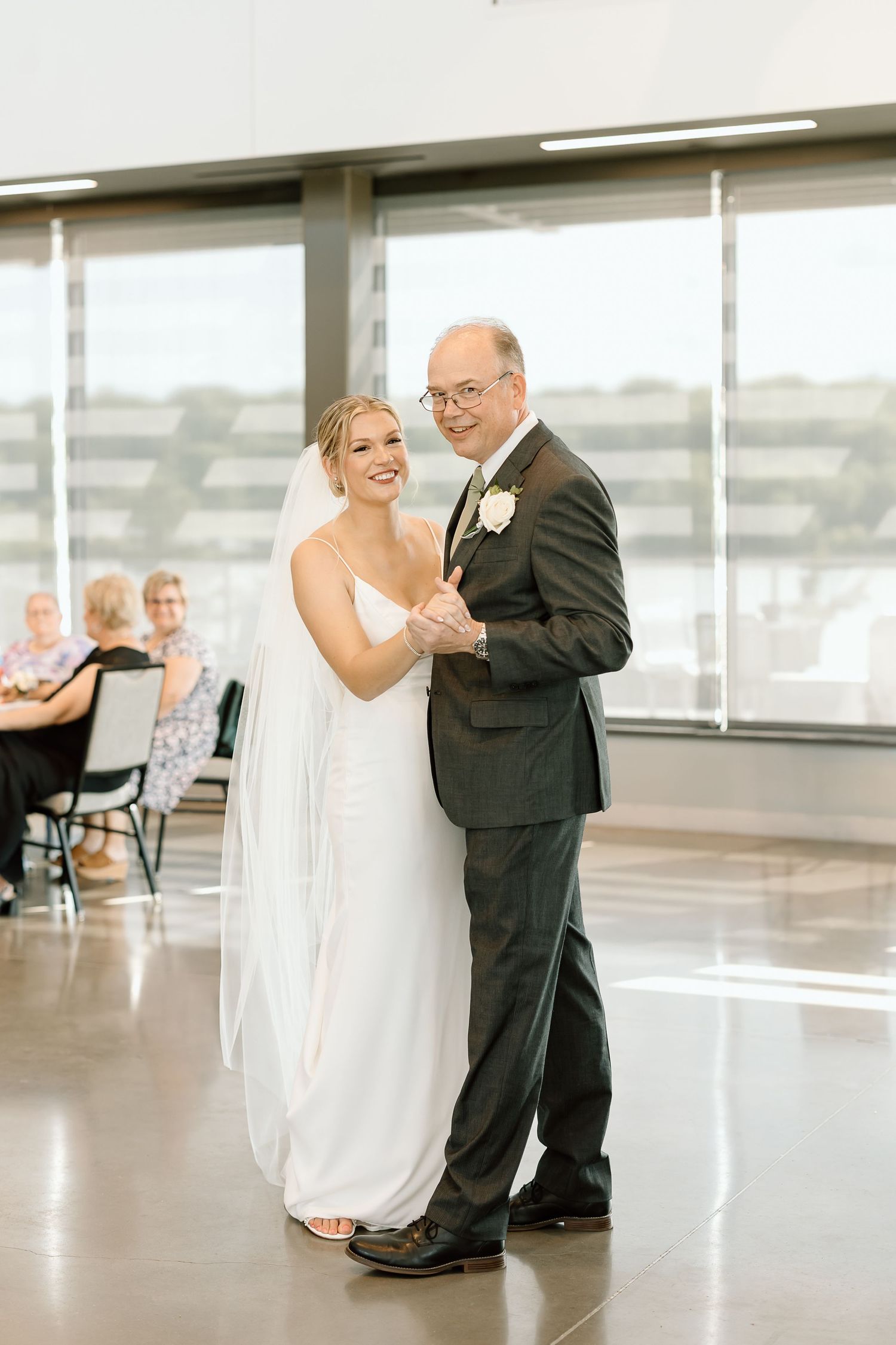 A couple dances together in a bright studio space with large windows and reflective floors.