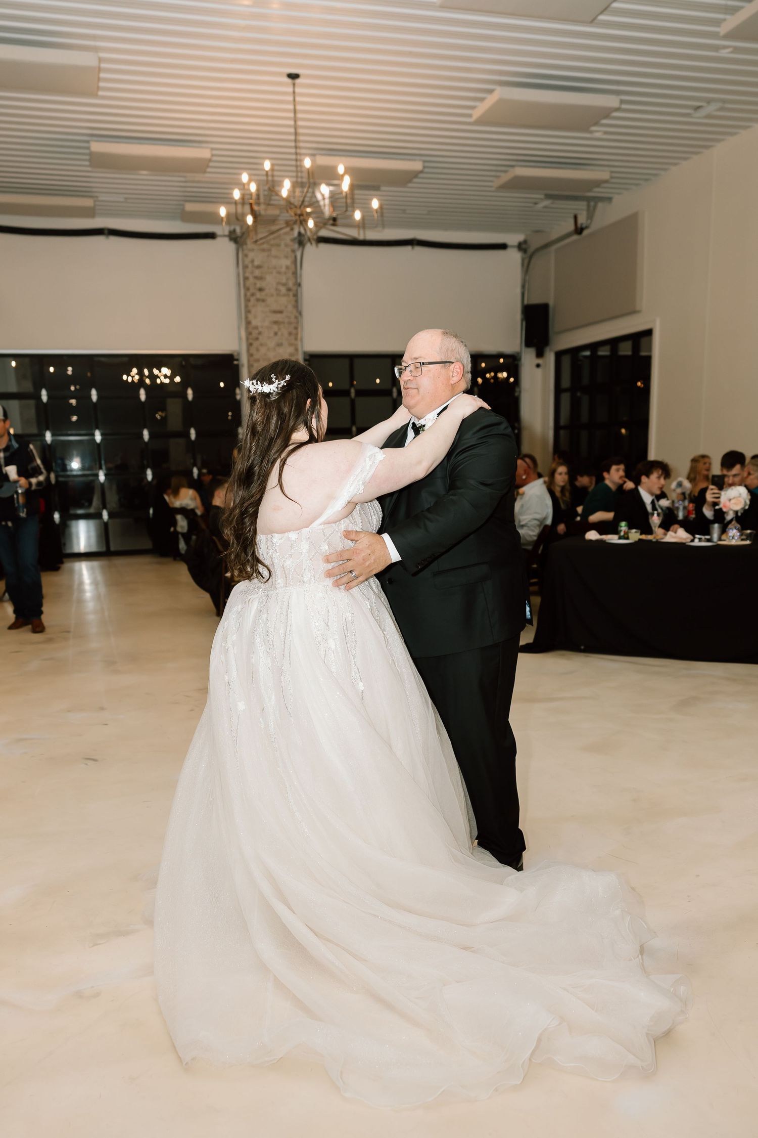 A couple performs an elegant dance during their wedding reception in a spacious white ballroom with pendant lighting.