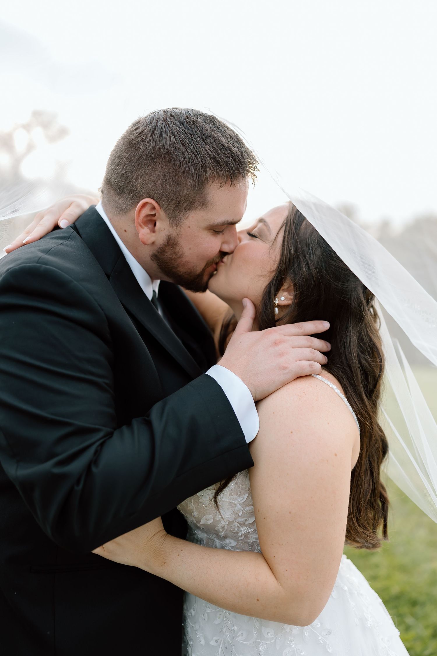 A romantic wedding kiss sequence showing four progressive moments captured outdoors.