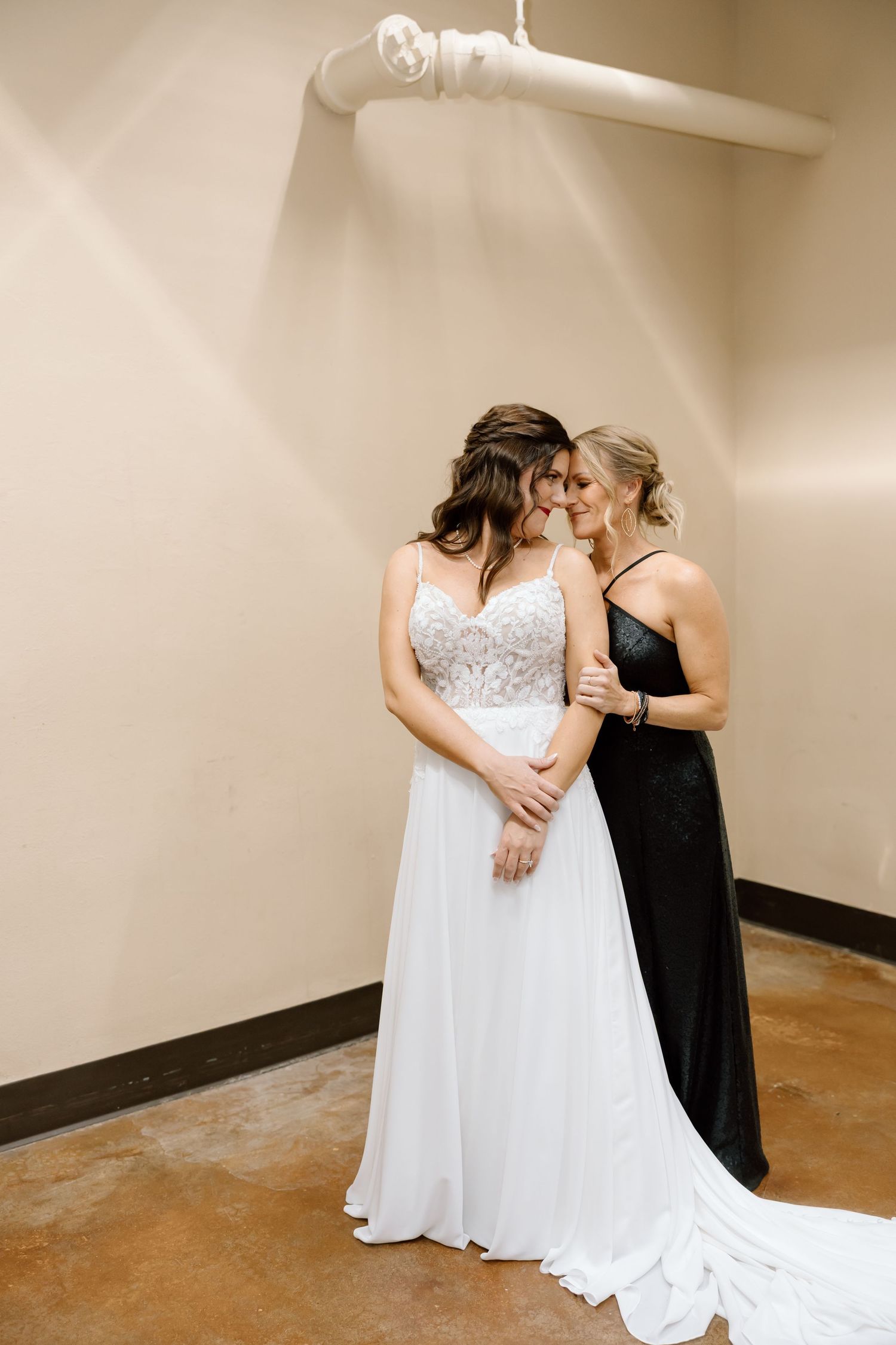 Two people share an intimate moment, one wearing a flowing white wedding gown and the other in an elegant black dress.