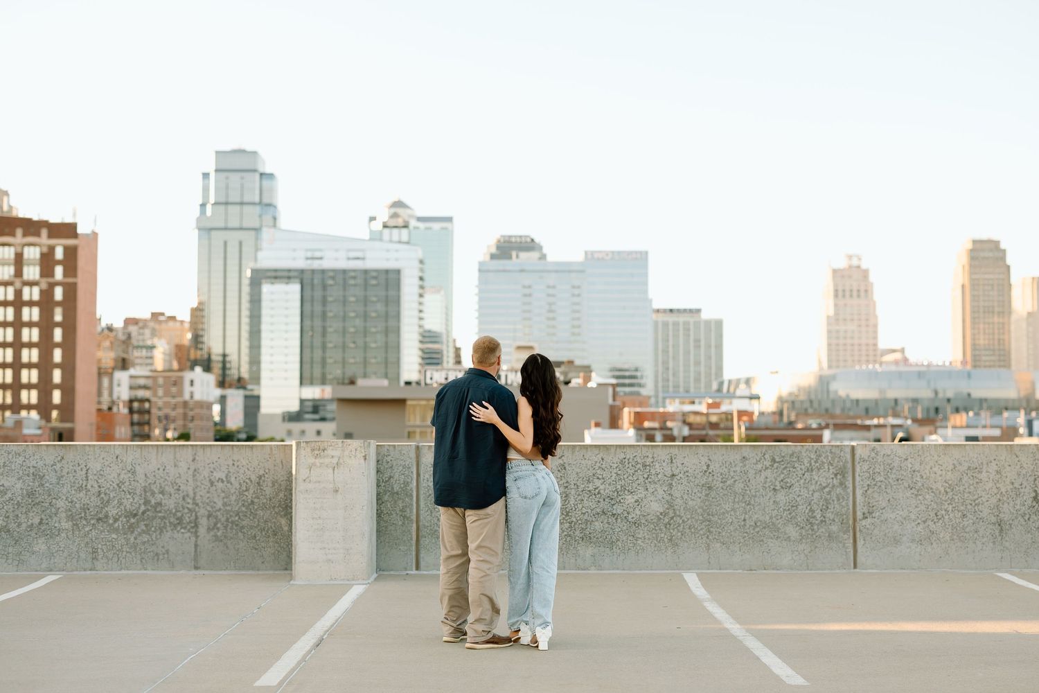 A couple stands on a rooftop overlooking the Kansas City skyline during golden hour.