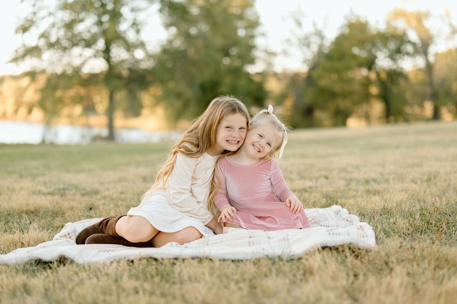 People laying on white blanket in grassy field during golden hour sunset.