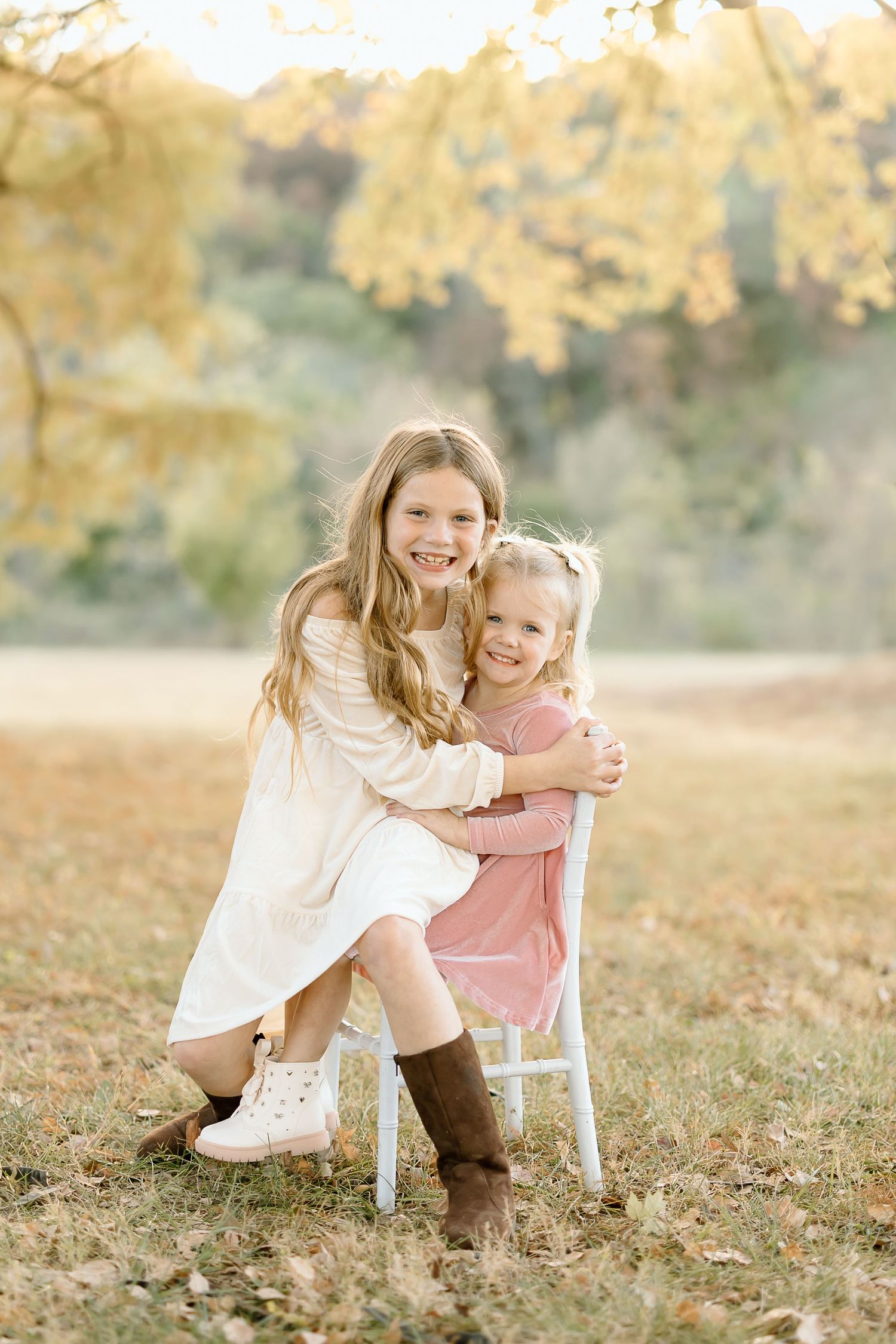 Two figures in a sunny autumn field share a sweet embrace while wearing boots and light-colored clothing.