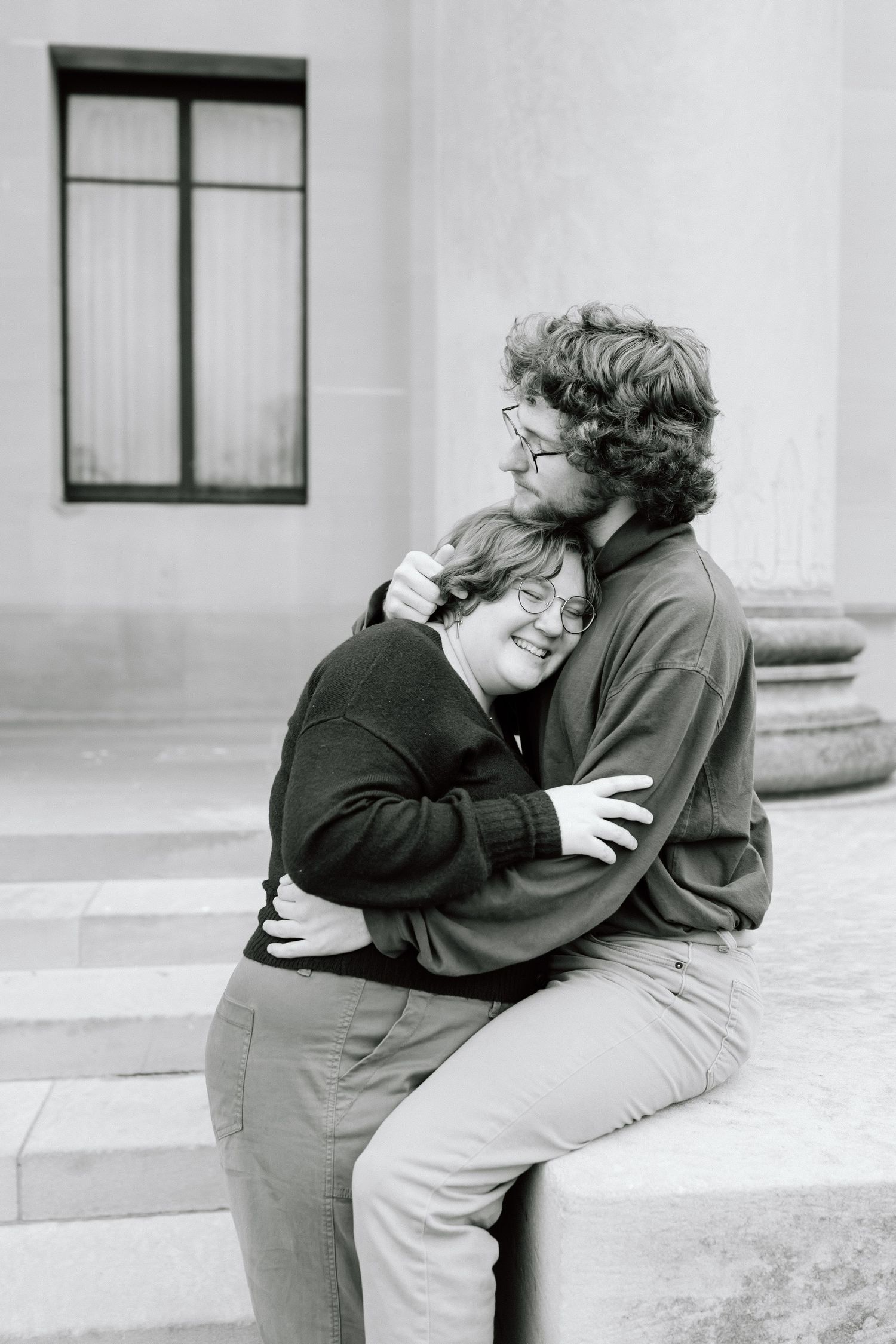 A tender black and white photograph of two people sharing an intimate embrace while sitting on stone steps.