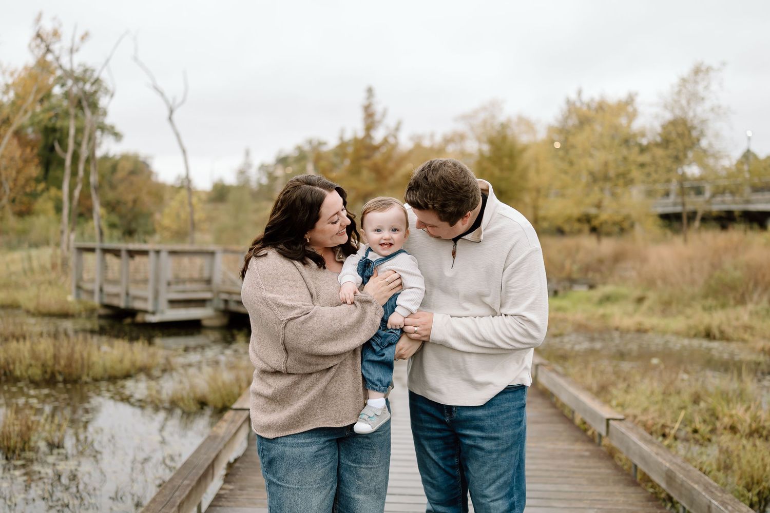 A couple shares a tender moment while walking along a wooden boardwalk through an autumn landscape.