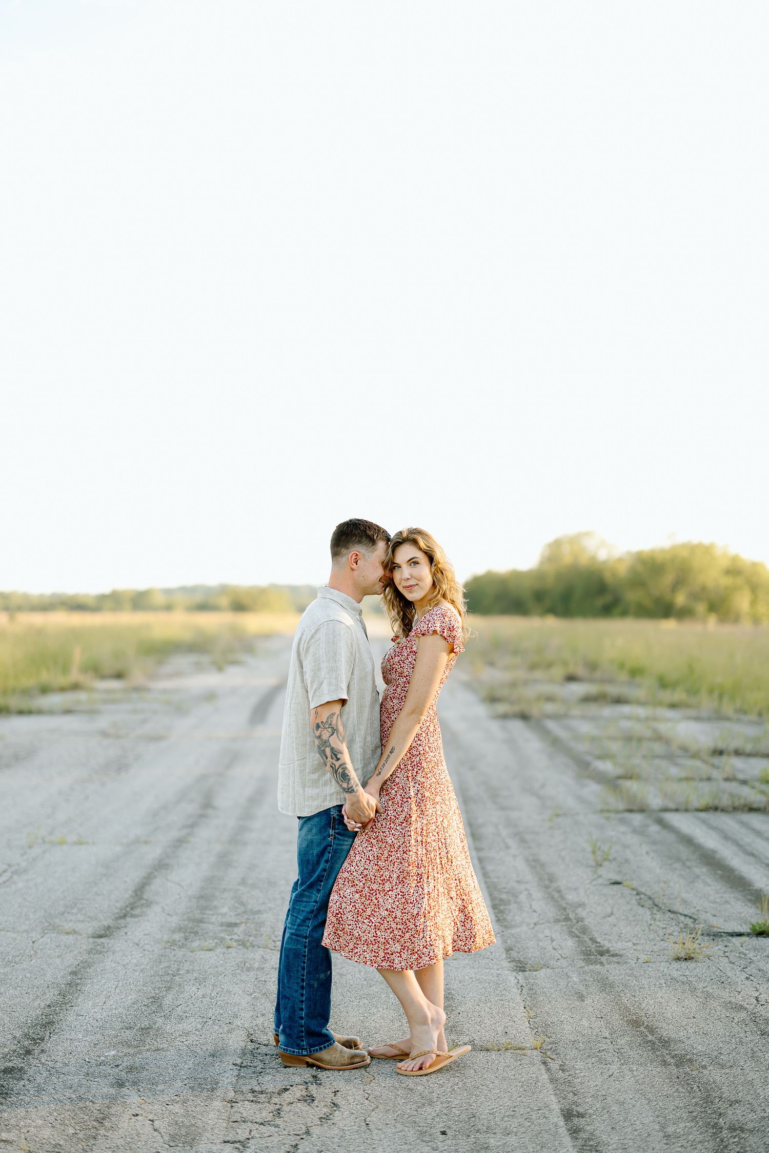 A romantic couple embraces on a rustic dirt road during a golden sunset photo session.