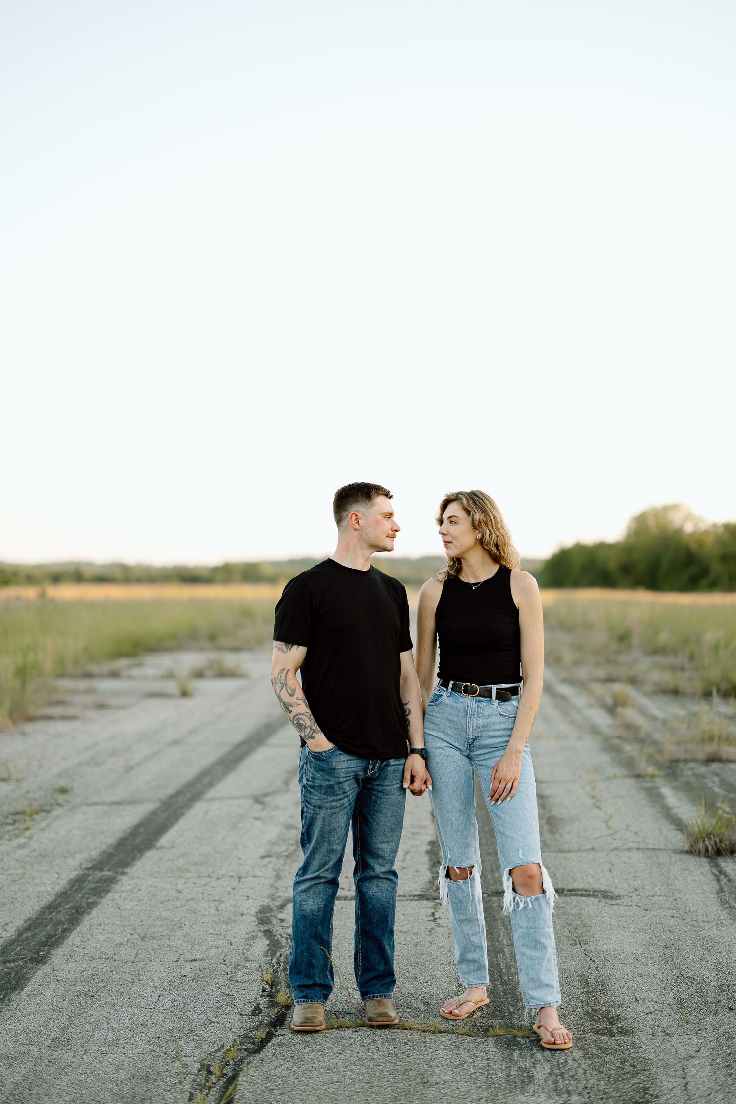 A couple in casual attire walking together on a rural dirt road at sunset.