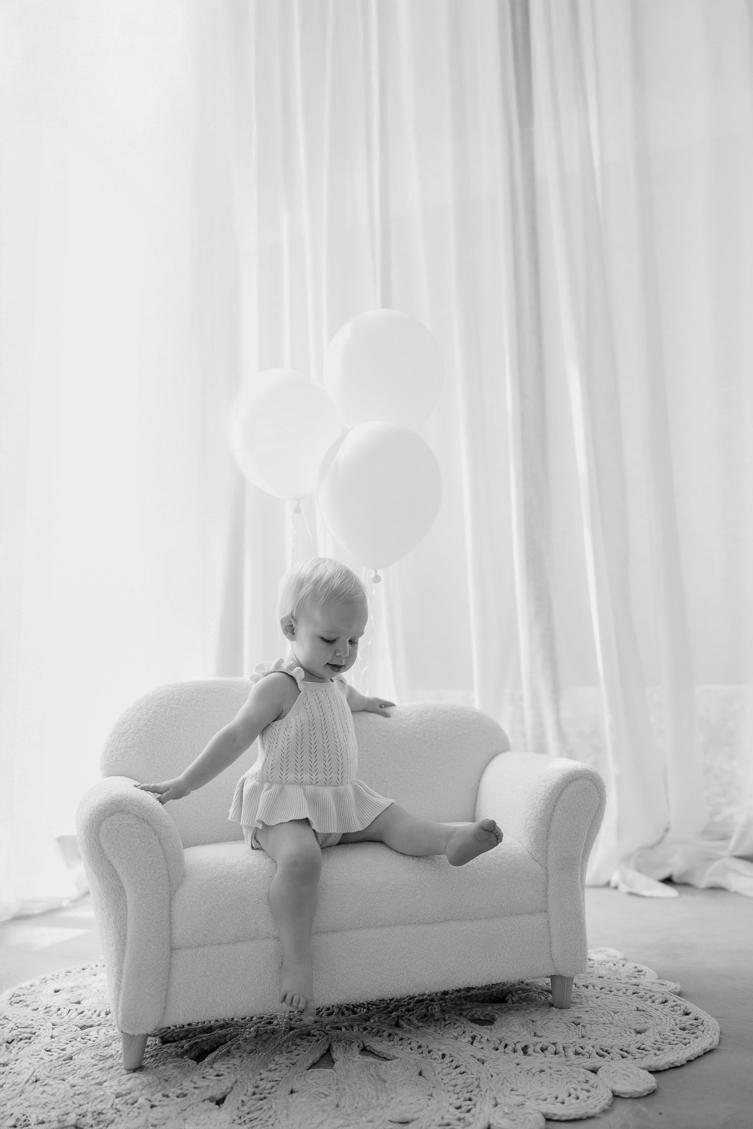 A series of four ethereal black and white photos showing a figure in white reclining on a sofa against light curtains.
