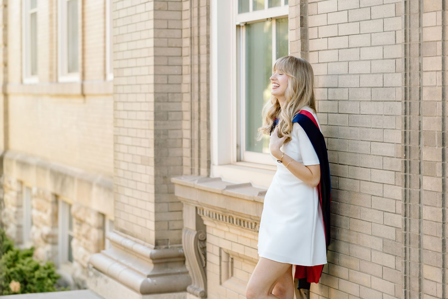A person in a white dress and black cardigan stands against a brick wall while holding a coffee cup.