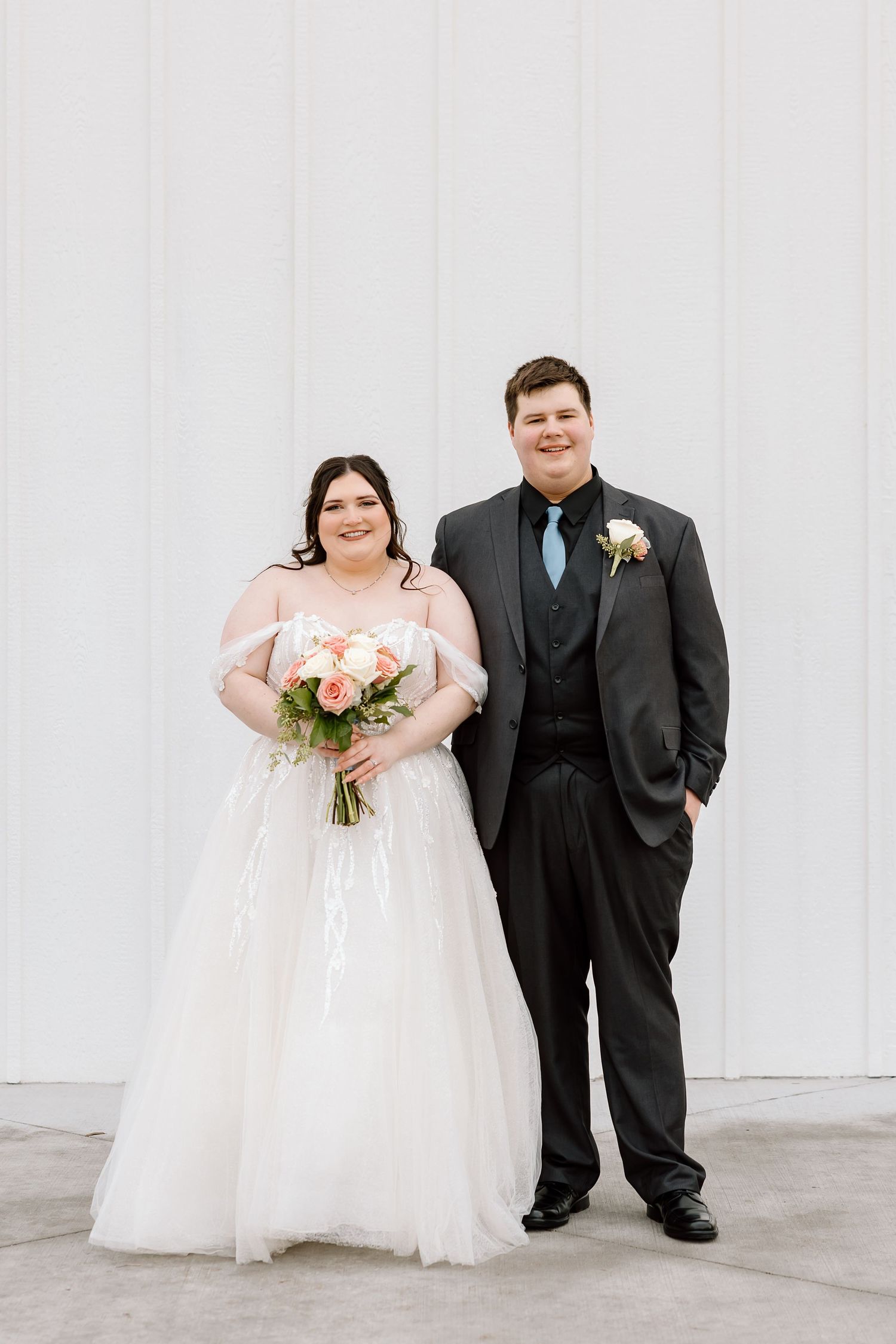 Newlywed couple posing formally against white wall at modern venue.
