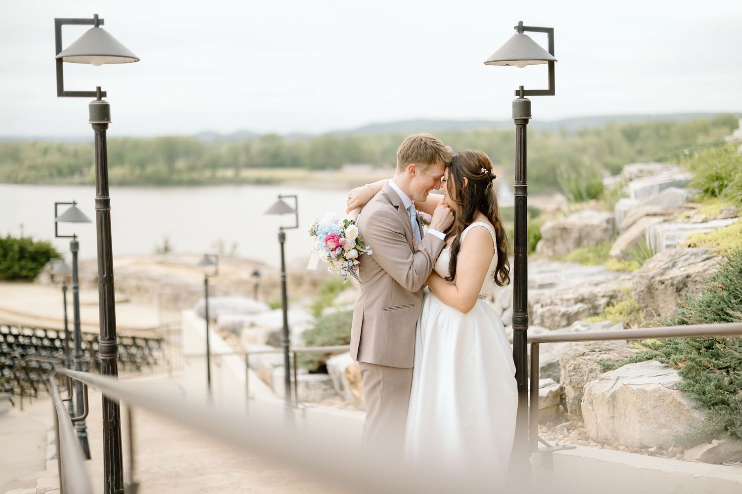 Romantic wedding photo on stone stairway with decorative lampposts.