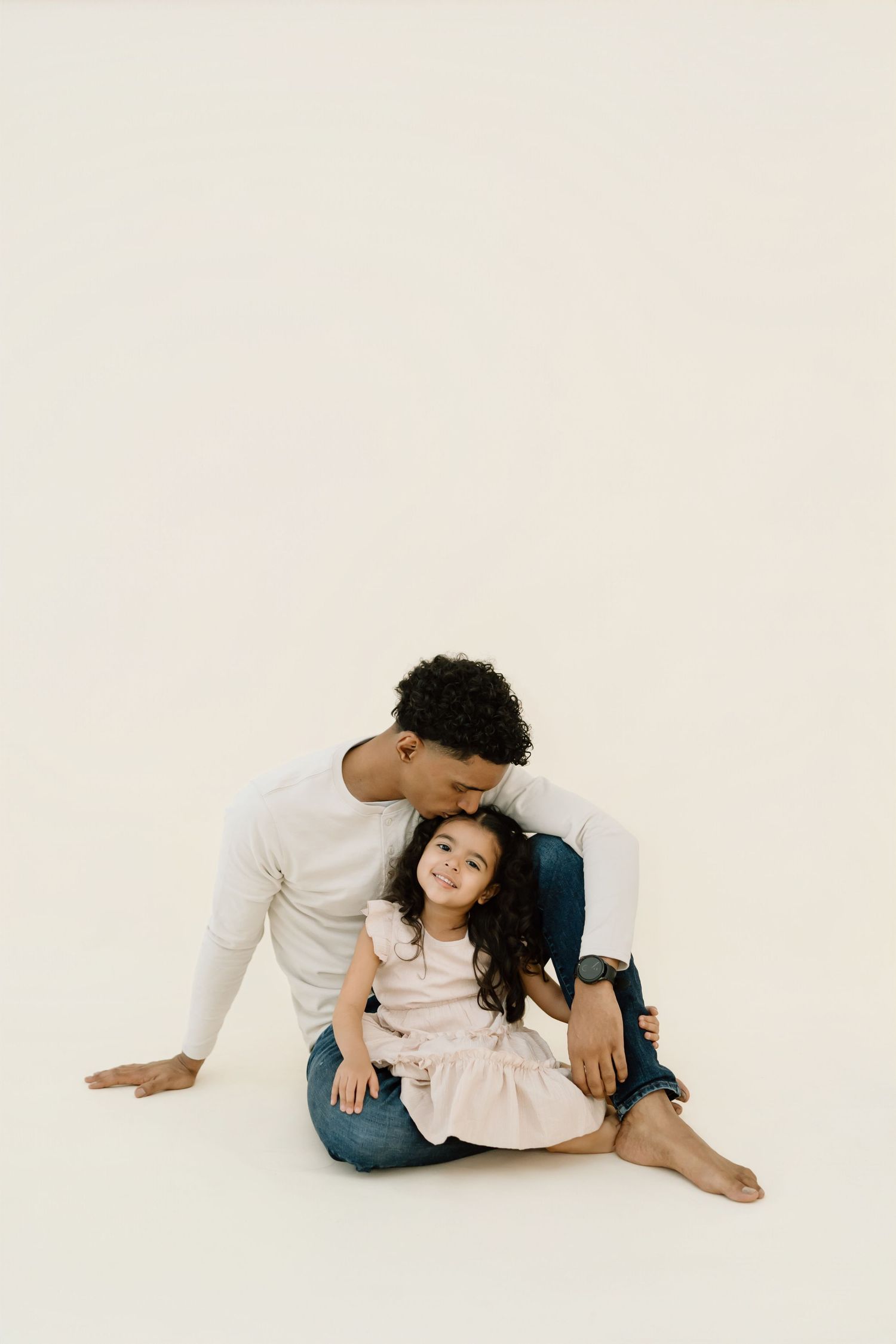 A tender moment between parent and child sitting together on a white backdrop in casual attire.