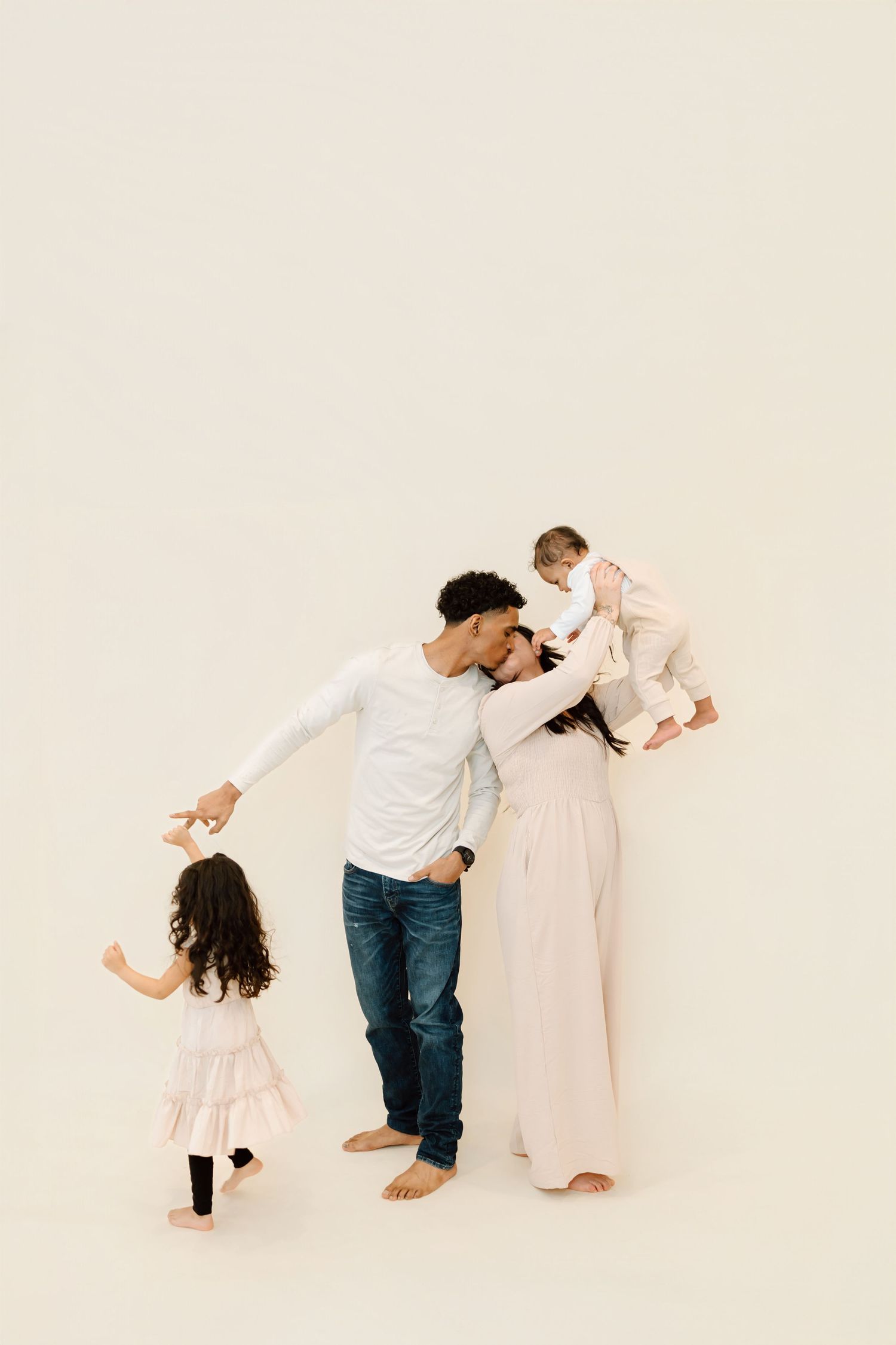 Three artistic photos show a family in white clothing playing and interacting against a light beige background.