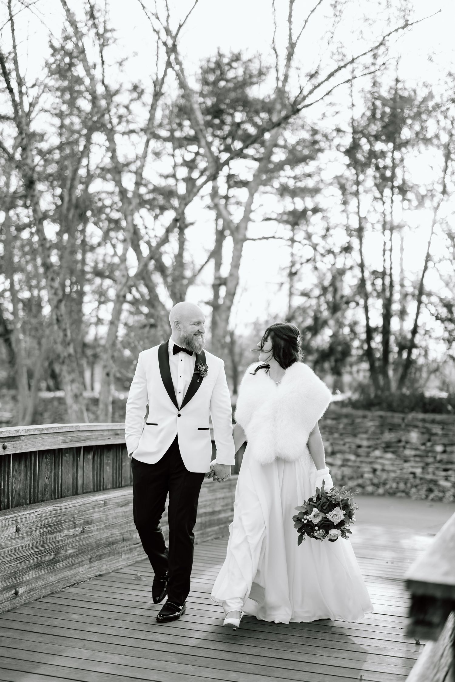 A romantic black and white wedding photo series showing a couple walking together on a wooden boardwalk.