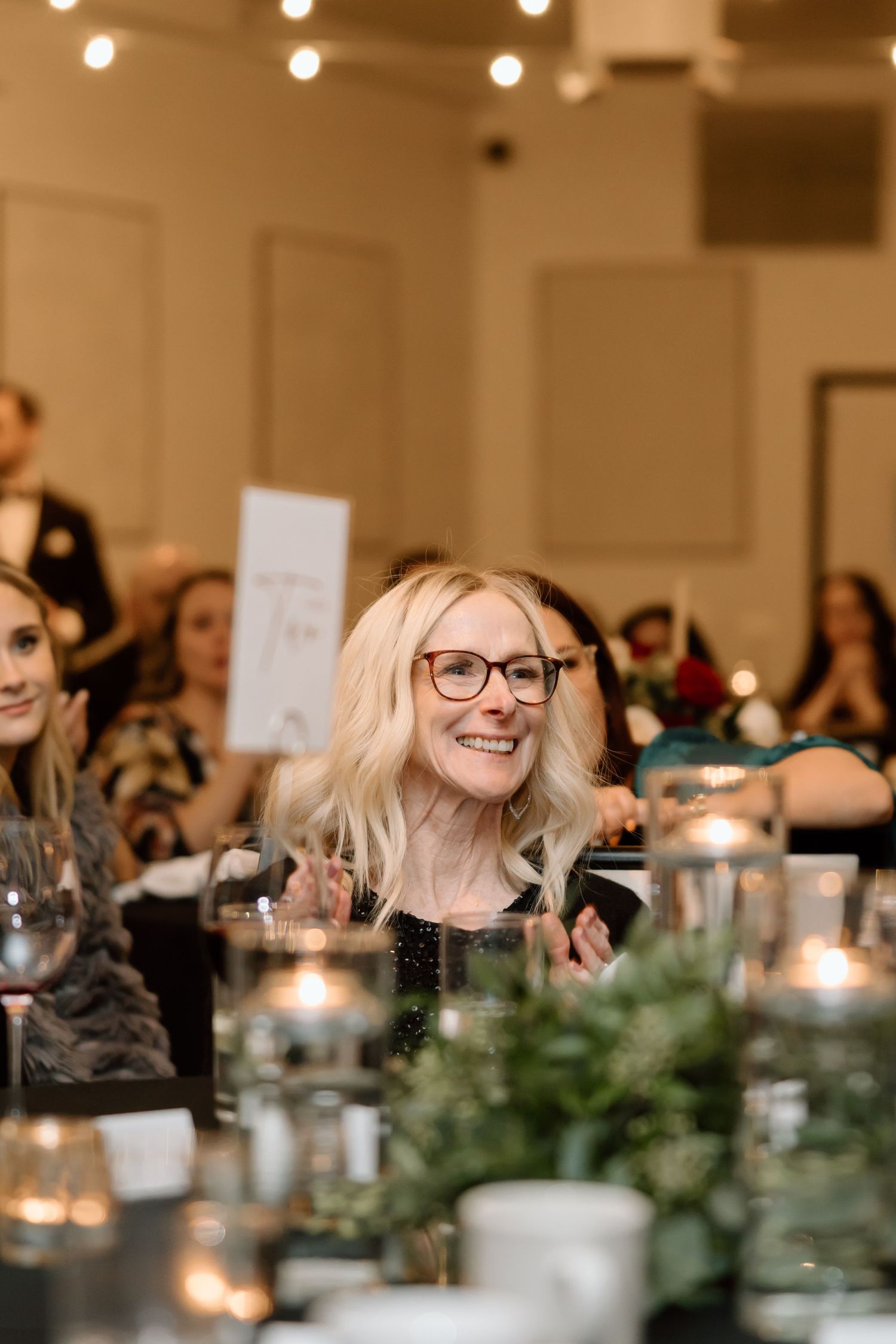 Wedding guests enjoy a candlelit reception dinner with greenery centerpieces and a warm, intimate atmosphere.