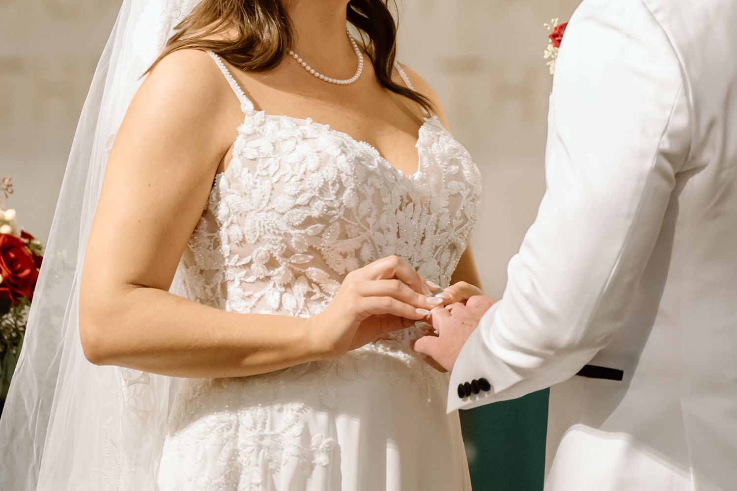 Close-up of hands exchanging wedding rings during ceremony with bride wearing delicate lace white gown.