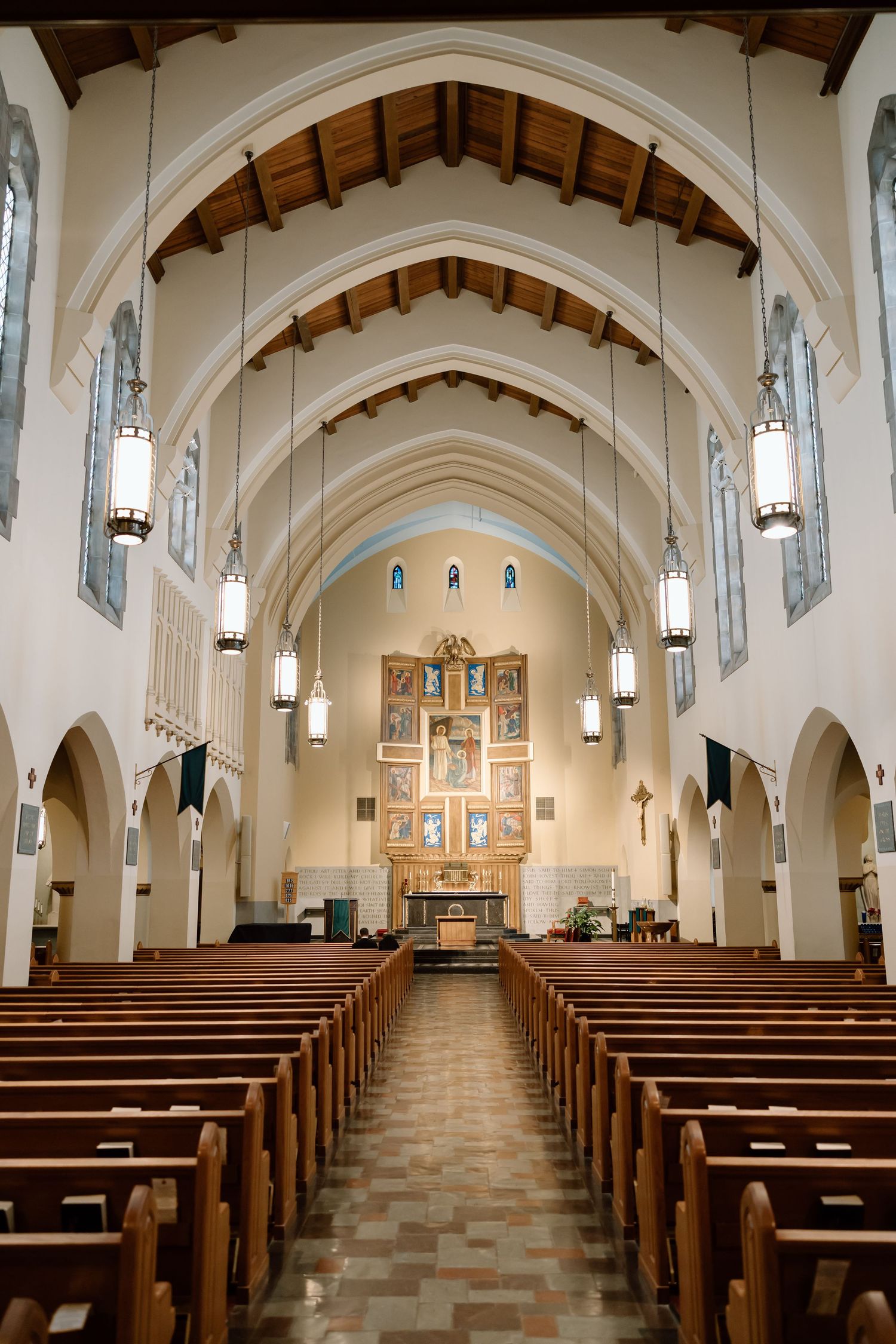 Interior view of a traditional church sanctuary with wooden pews, vaulted arches, and hanging pendant lights leading to an altar.