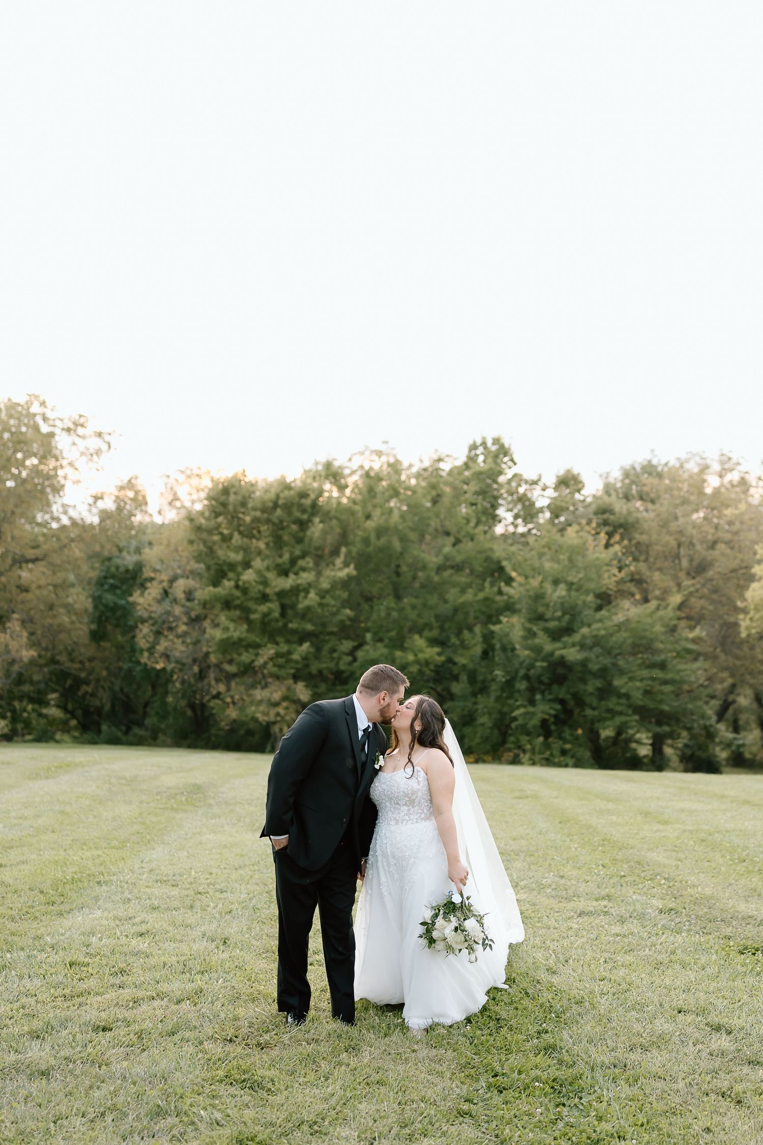 Bride and groom share an intimate moment on a grassy hillside during golden hour.