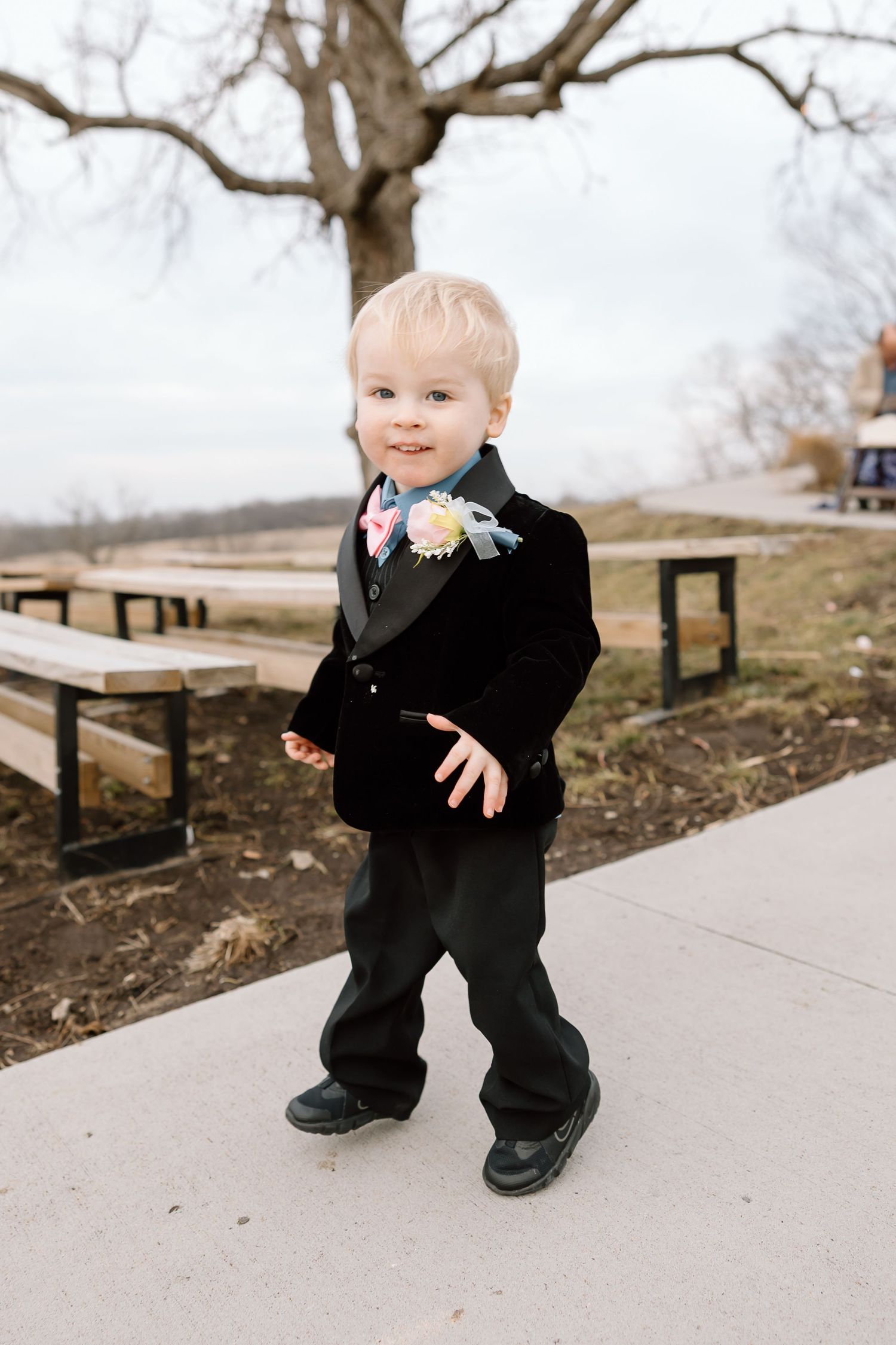 A small child in a black suit plays on a concrete path in a park during winter.