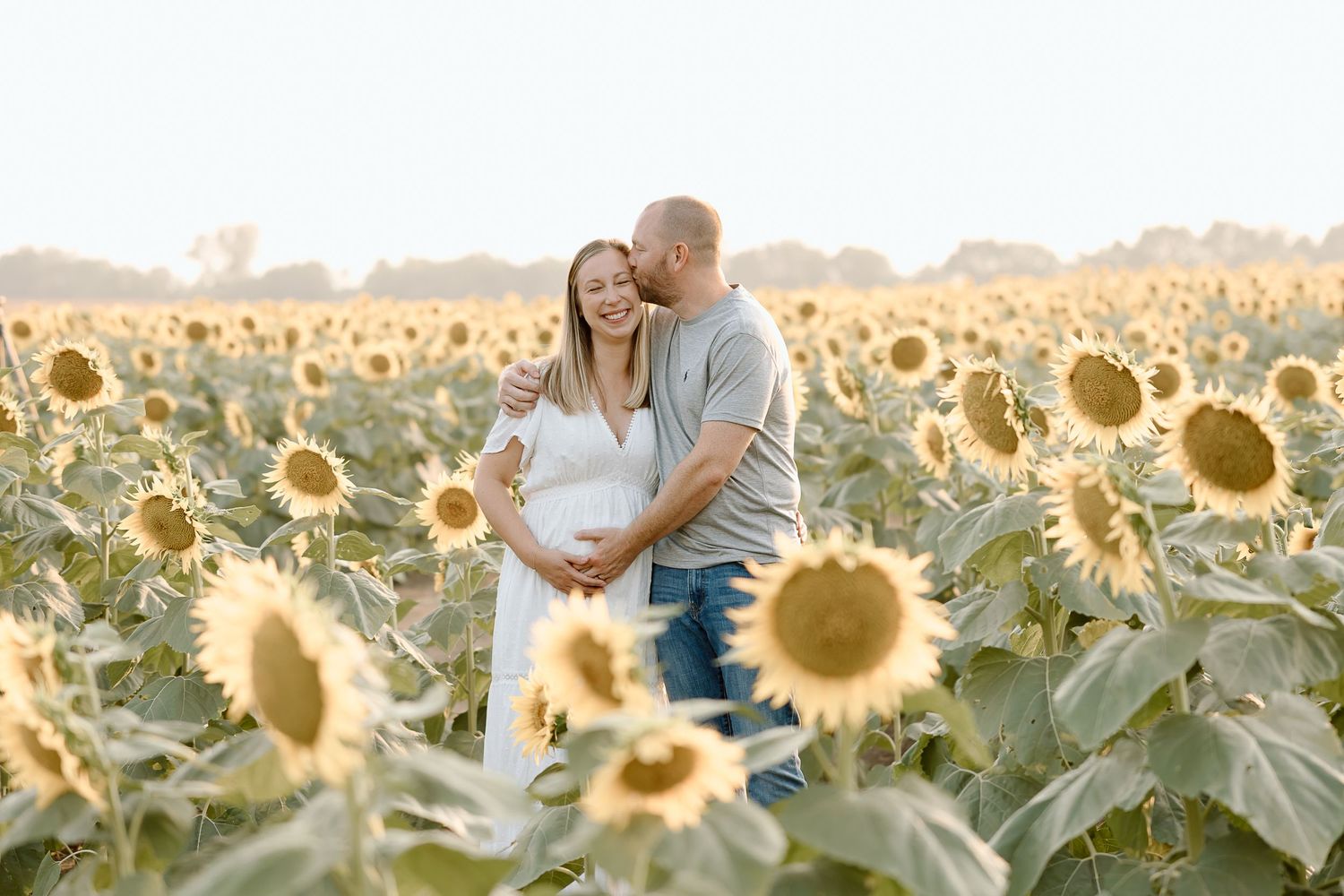 A couple embraces in a golden sunflower field during sunset creating a romantic silhouette against the warm sky.