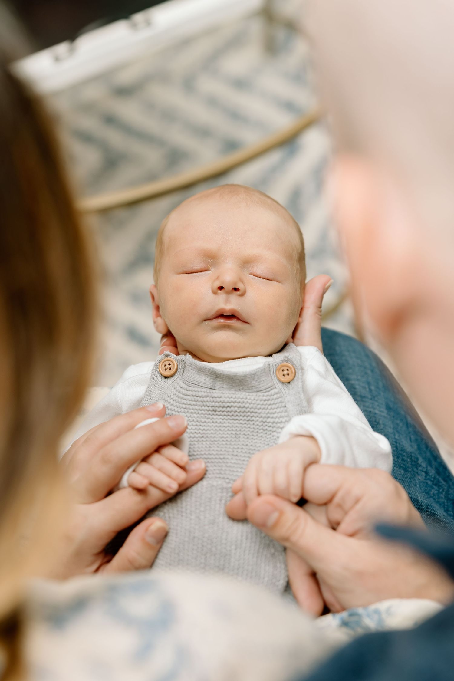 A sleeping newborn baby wearing a gray outfit rests peacefully while being cradled in someone's arms.