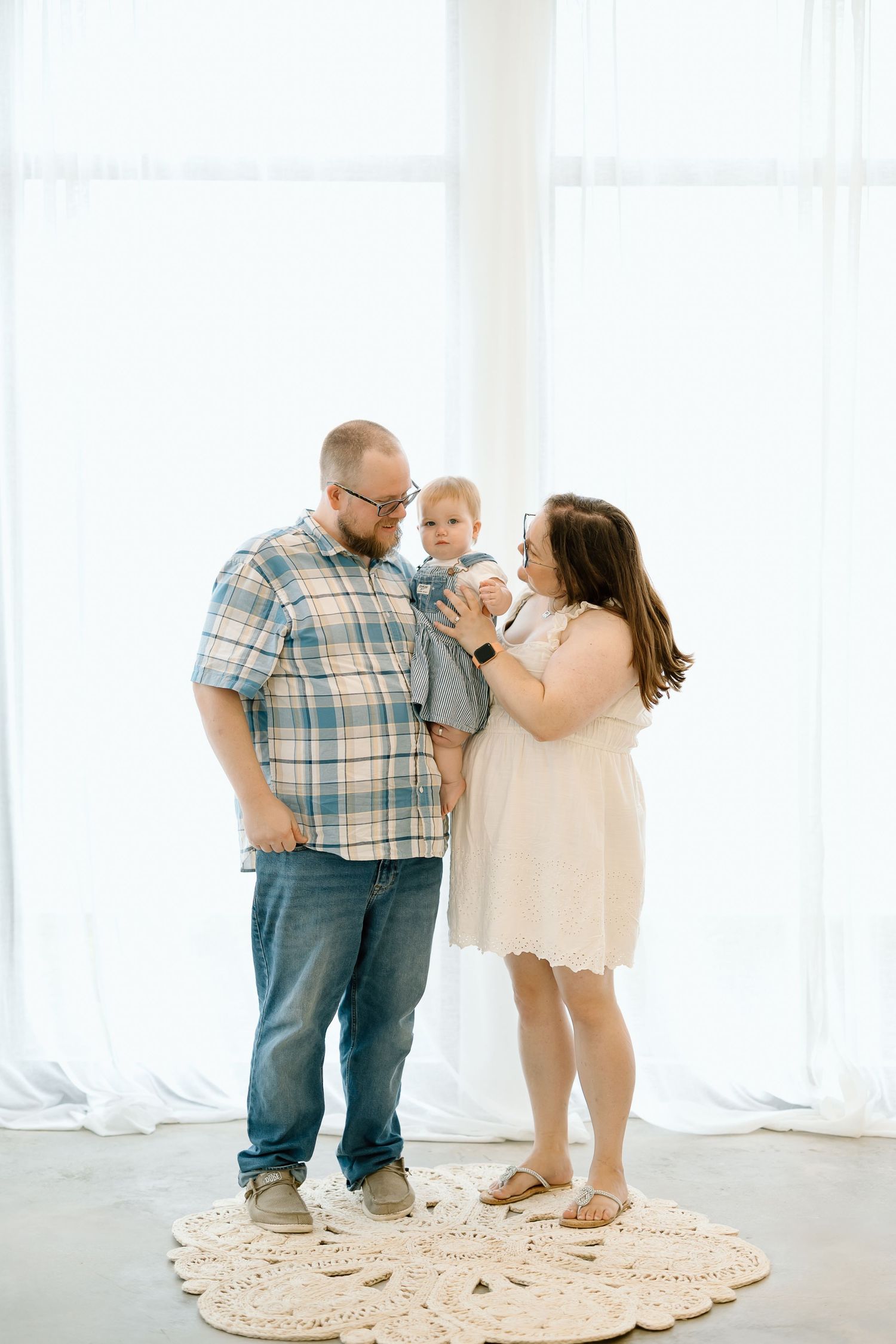A family shares tender moments together on a round cream-colored rug in a bright white studio setting.